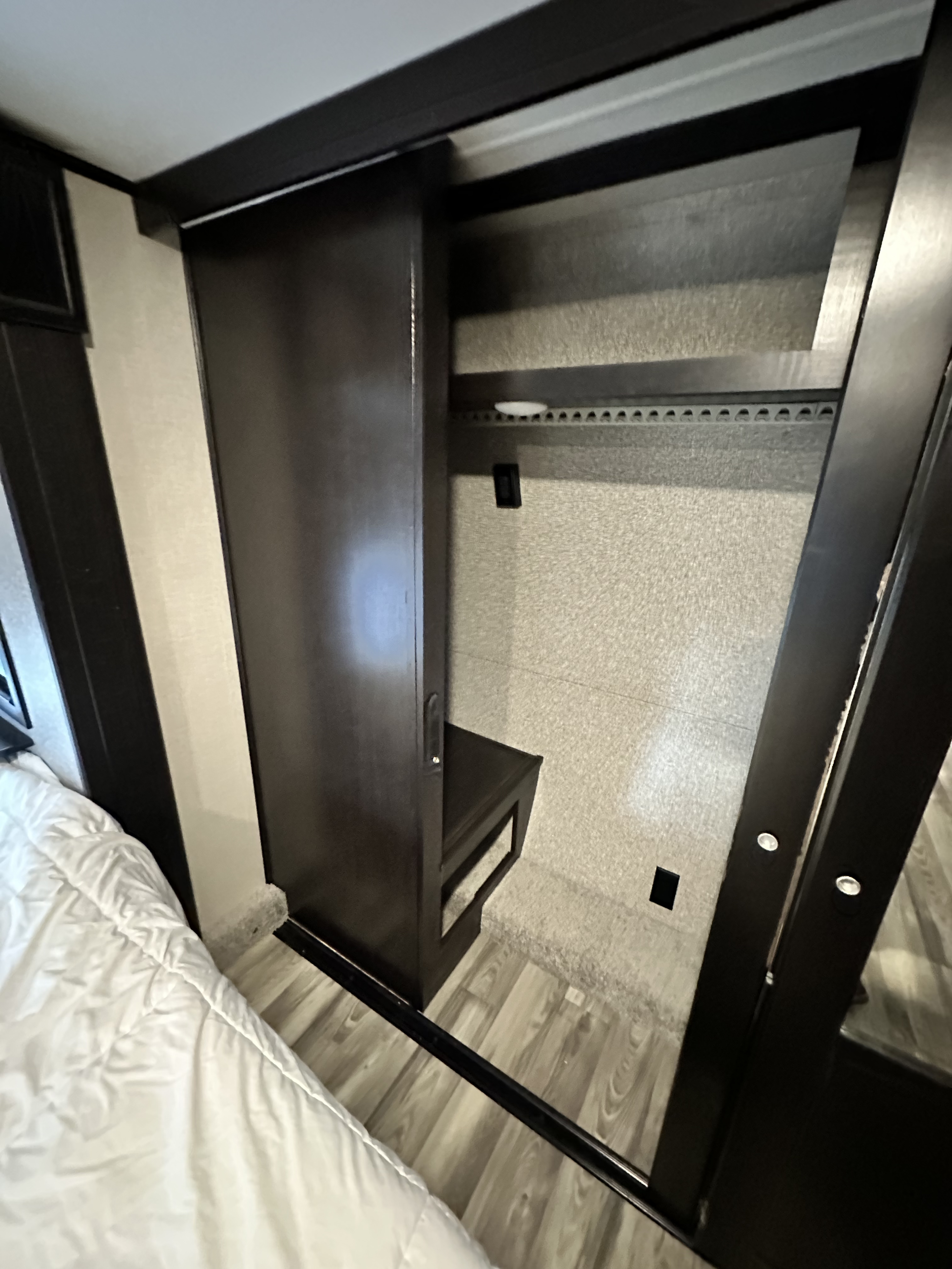 RV rental bedroom features: a dark wood wardrobe with sliding door, interior shelves, and pull-out bench, next to a comfy bed.. Highland Ridge RV Open Range 2022