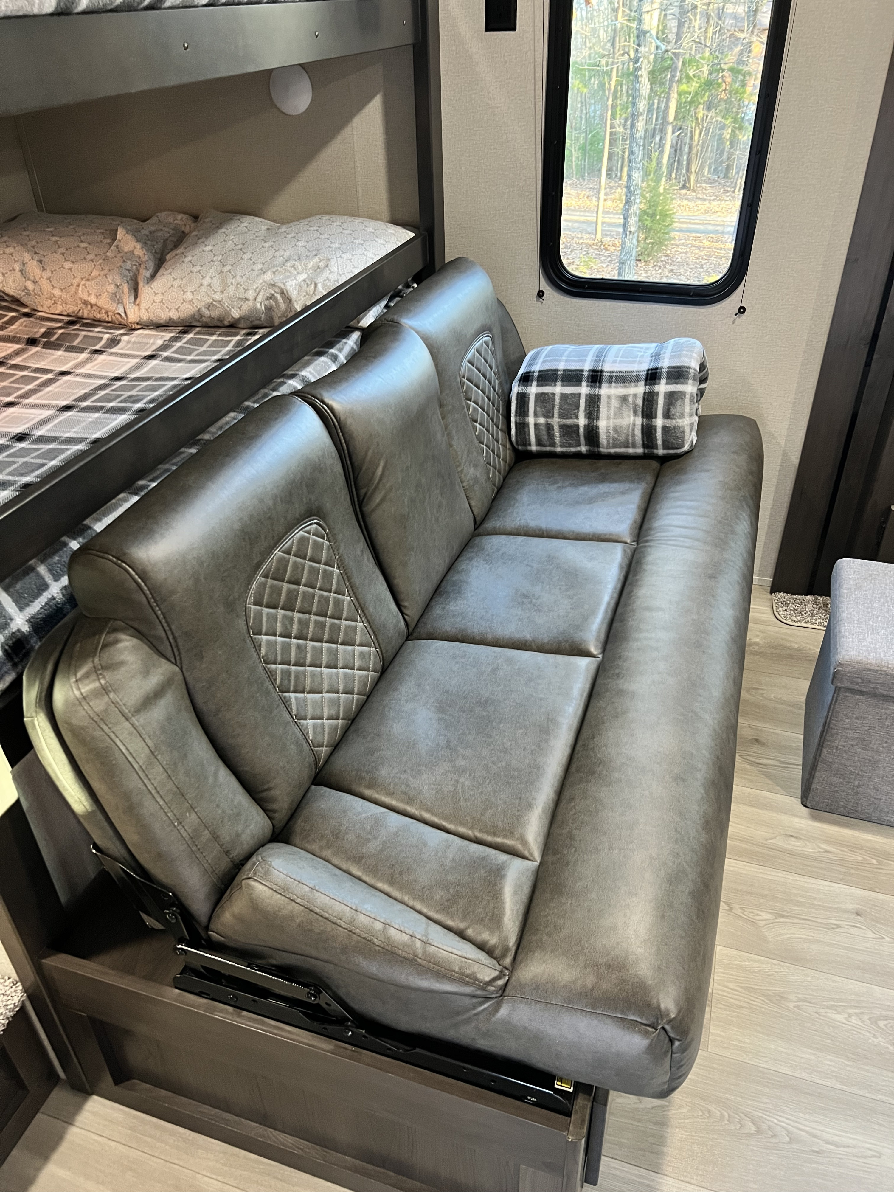 RV rental interior featuring a cozy reclining sofa, bunk beds, and a view of the outdoors.. Grand Design Transcend Xplor 2023