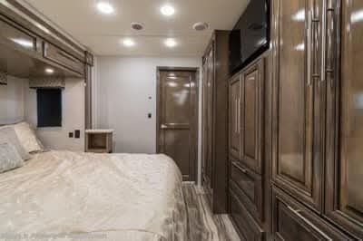 Inside a modern RV rental bedroom featuring a large bed, overhead cabinets, wall storage, and a TV for travel comfort.. Forest River Georgetown 2022