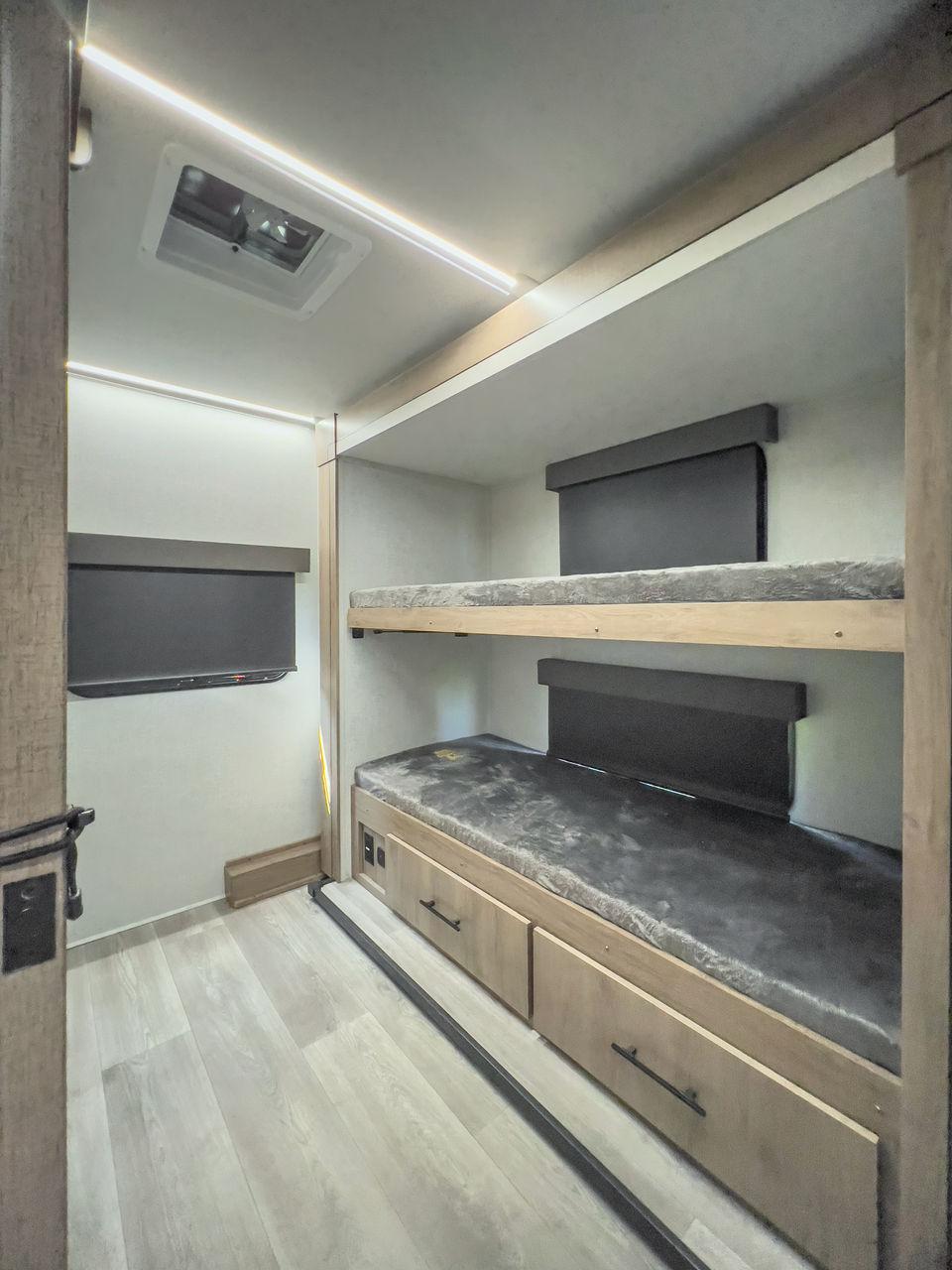 RV rental's bunk area: two beds with gray mattresses, storage drawers, wall-mounted TV, and bright LED lights.. Grand Design Imagine XLS 2024