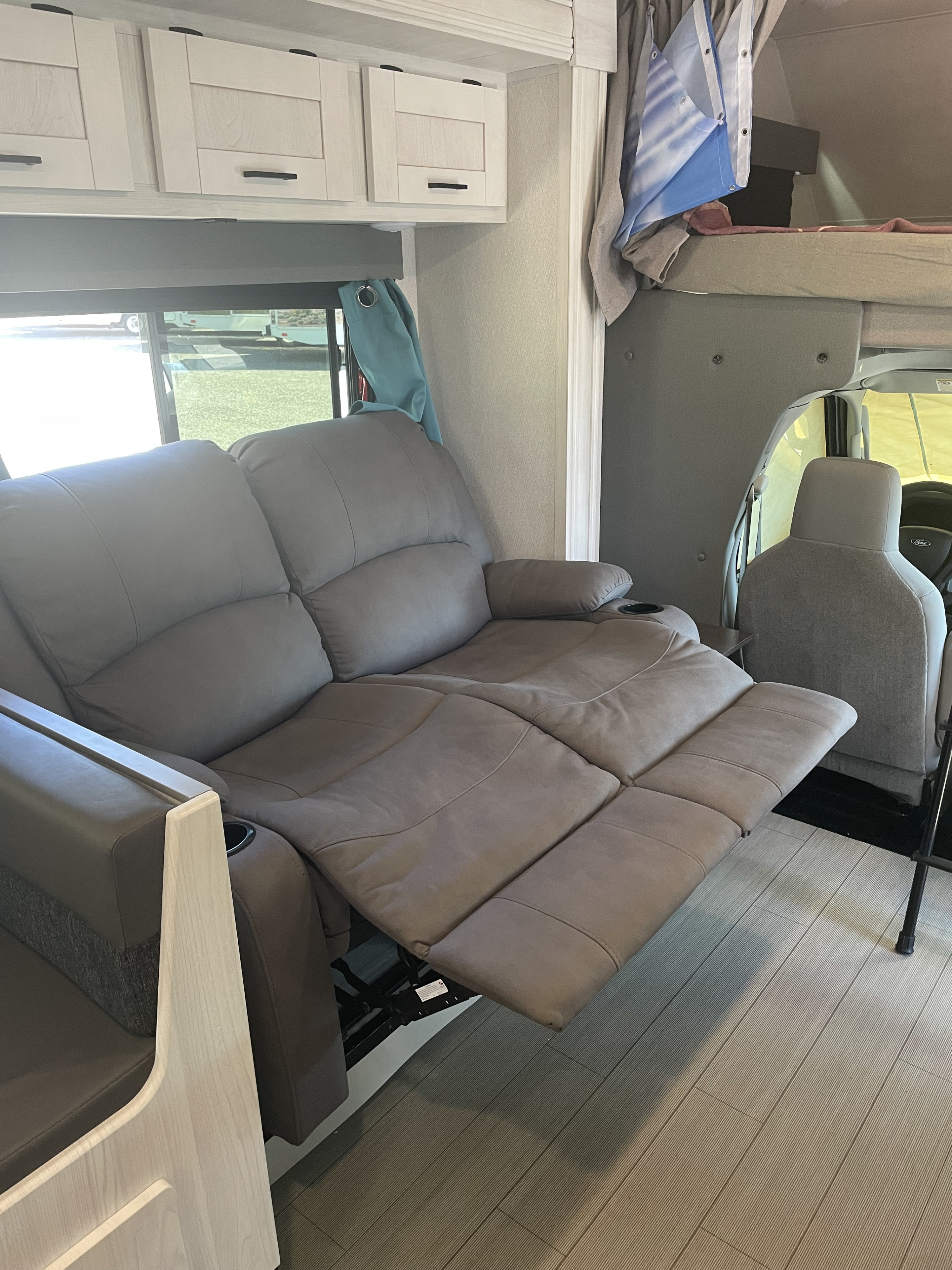 Spacious RV rental interior: grey reclining theater seating, light cabinets, and bunk over cab. Enjoy comfort on the road.. East to West Entrada 2023