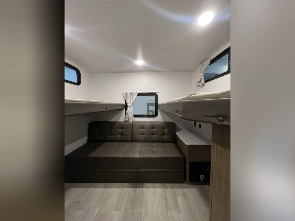 This RV rental interior features a convertible sofa, two bunk beds, and windows, maximizing sleeping and living space.. Forest River Wildwood X-Lite 2025