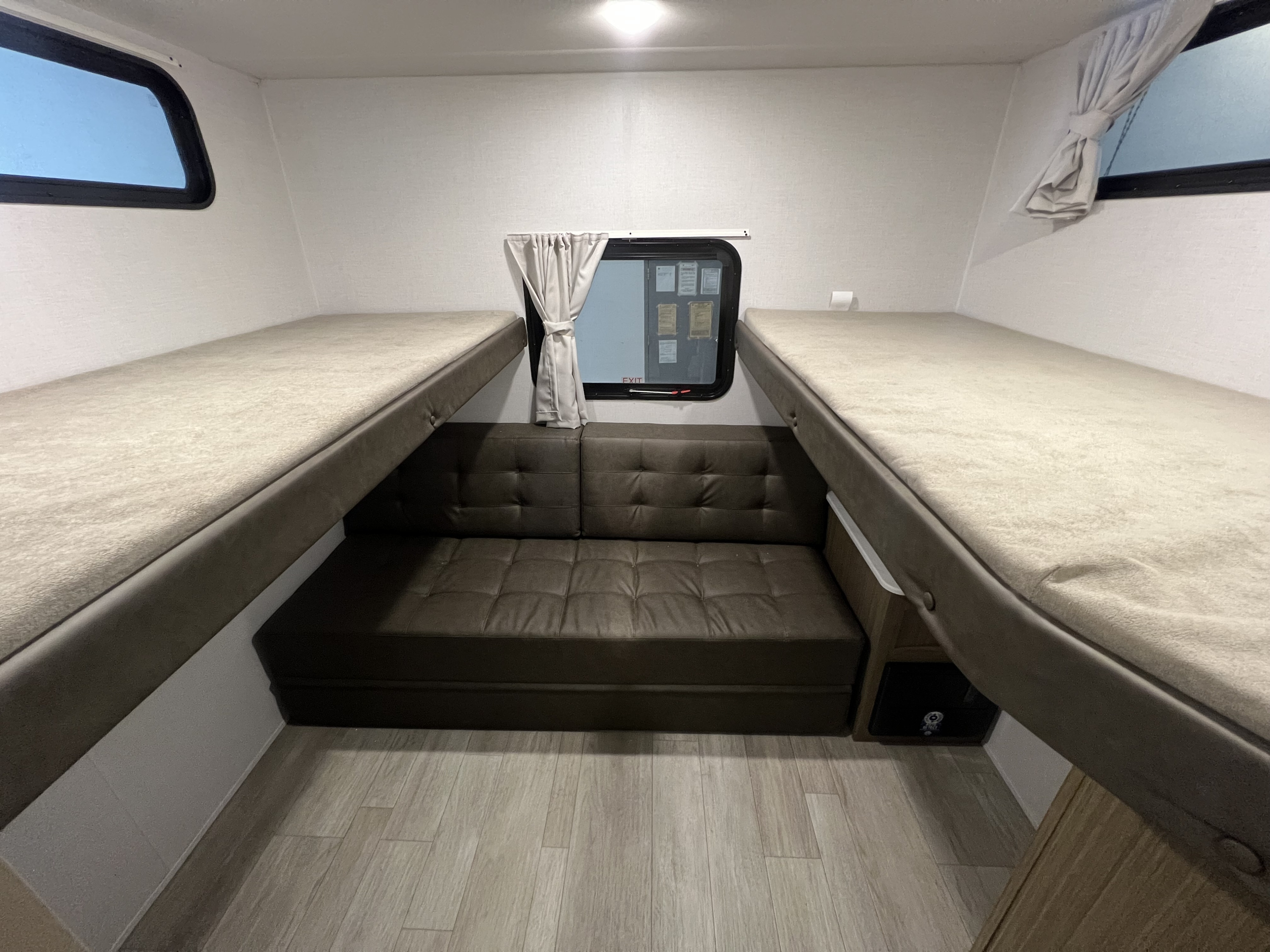 RV rental interior: two cozy bunk beds flank a central sofa and window, offering a compact sleeping and lounge space.. Forest River Wildwood X-Lite 2025