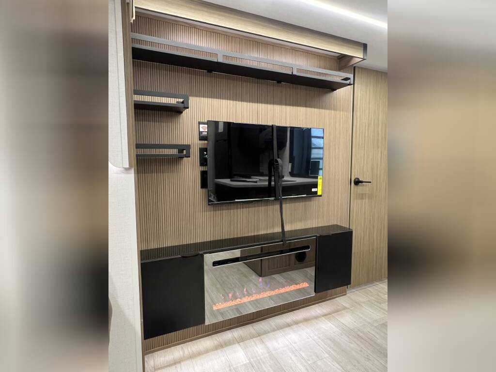 Modern RV rental: Integrated entertainment unit with a TV, electric fireplace, and shelves set against a slatted wall.. Forest River Wildwood X-Lite 2025