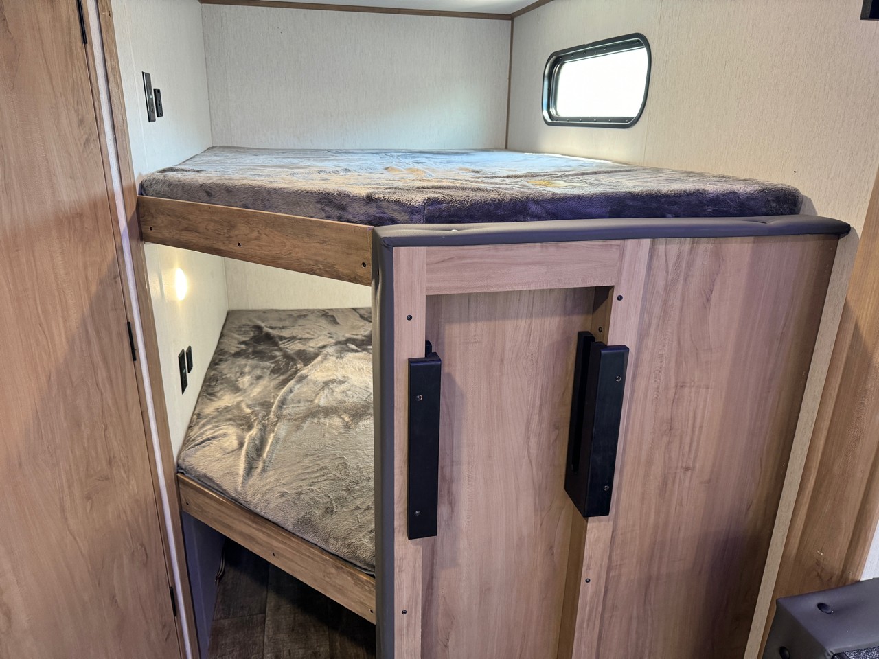 Cozy RV rental bunk beds with wooden frames and soft blankets, complete with lighting and a window. Perfect for family trips.. Forest River Cherokee Alpha Wolf 2023