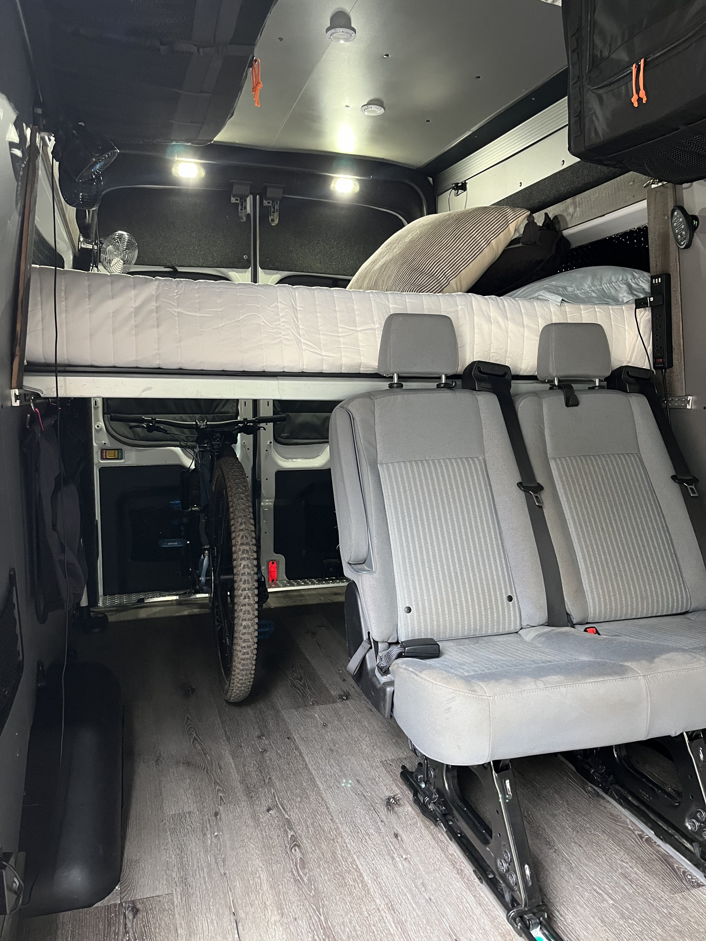 Interior of an RV rental: A raised bed above two passenger seats, with a mountain bike stored below. Practical camper van setup.. Ford F350 2015