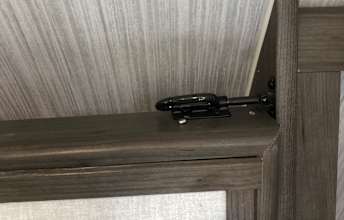 An RV rental interior view shows a black, metal latch on a dark wood-grained trim, likely securing a window or cabinet.. Coachmen Clipper 2022