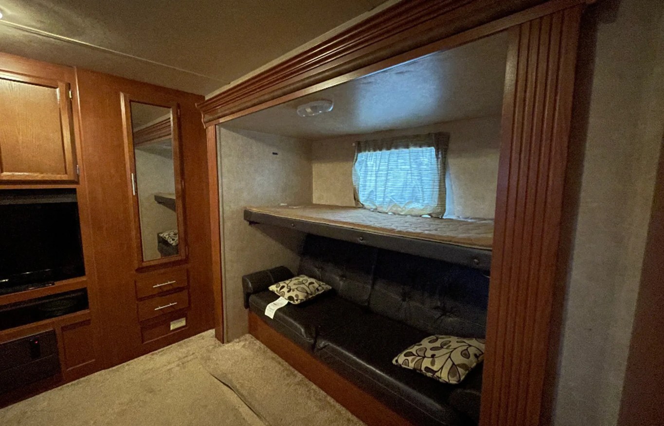 RV rental interior: bunk beds with a window, a black futon sofa, and wood cabinetry with TV & mirror. Compact living.. Forest River Salem 2014