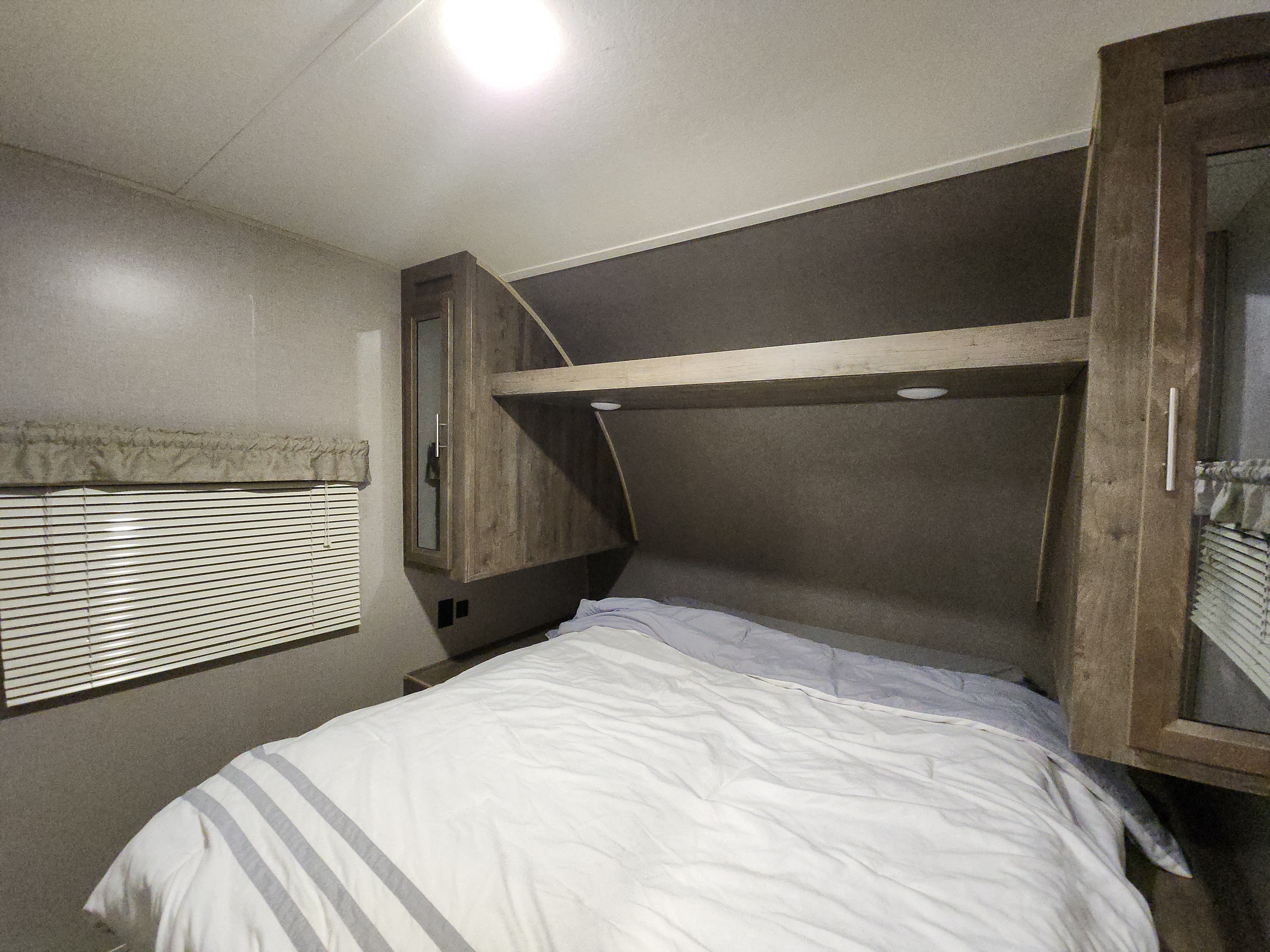 Cozy RV rental bedroom with a bed, wooden storage, recessed lighting, and a window with blinds.. Forest River Aurora Aurora 2021