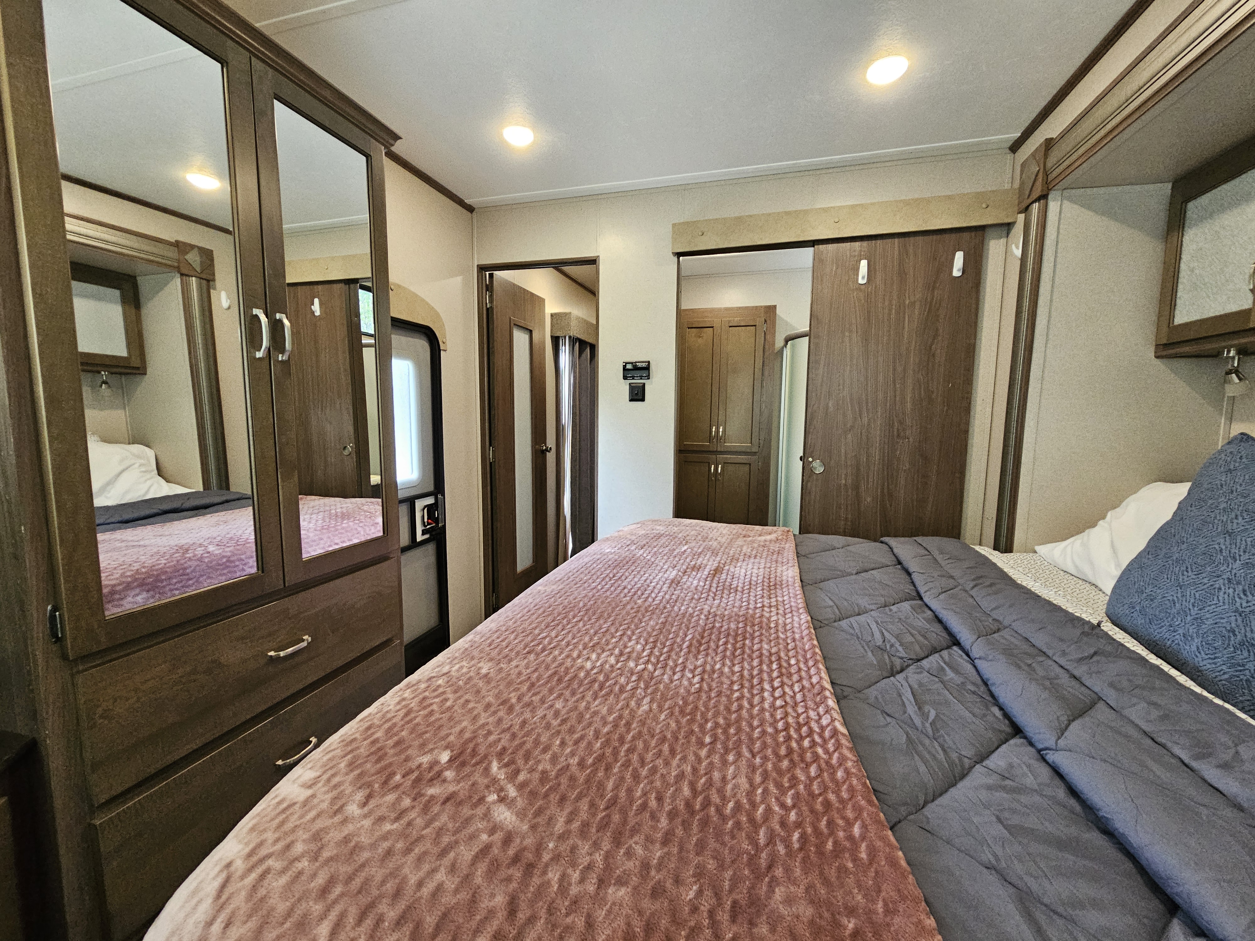 RV rental bedroom featuring a cozy bed with pink and gray bedding, a mirrored wardrobe, and compact design for travel comfort.. Keystone Retreat 2019