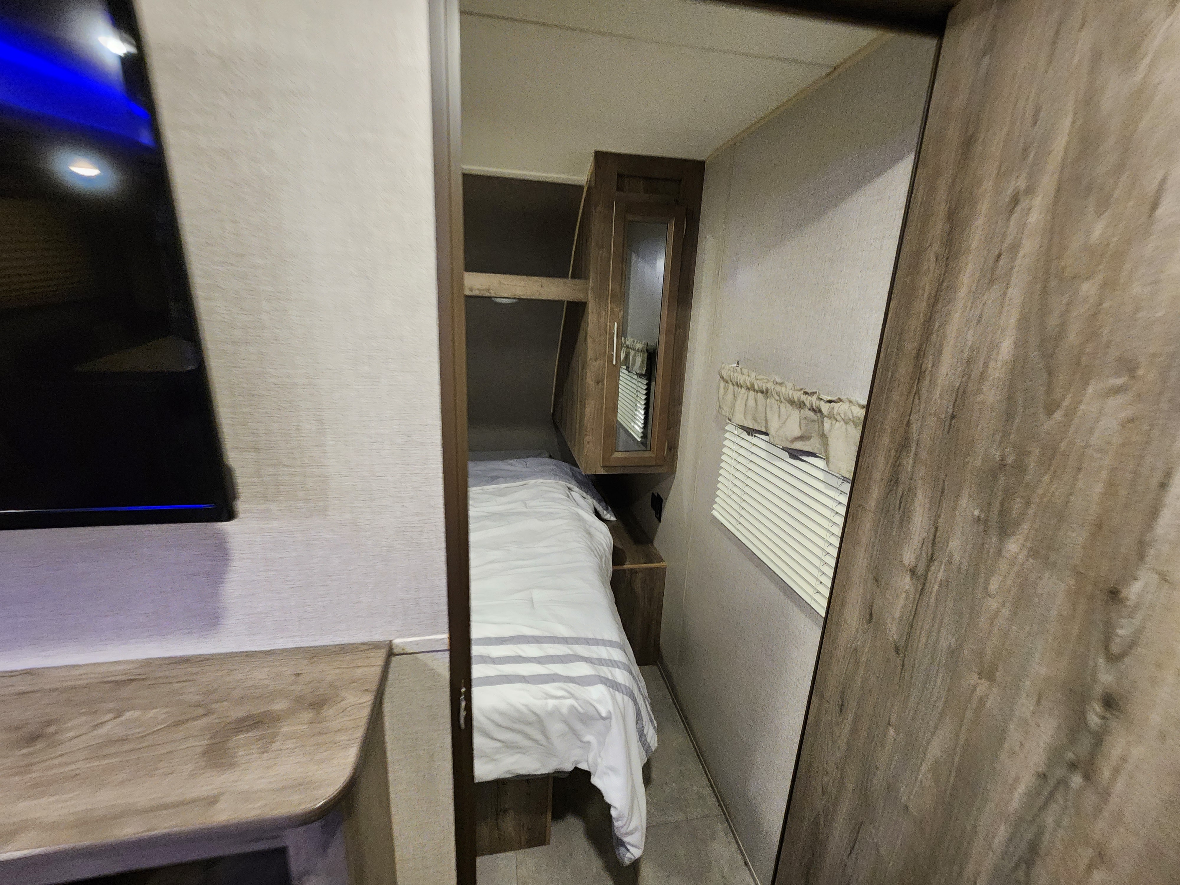 This RV rental bedroom offers a cozy bed, window, and a TV on the left.. Forest River Aurora Aurora 2021