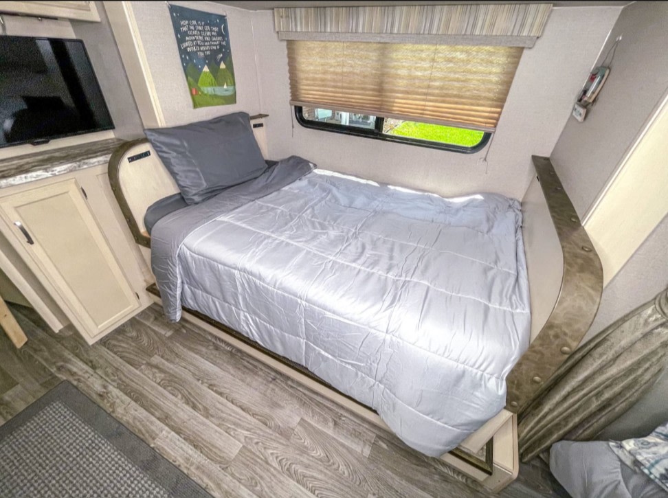 Cozy RV rental bedroom featuring a made bed with gray linens, TV, cabinets, and a window with a shade.. Winnebago Micro Mini 2306BHS 2019