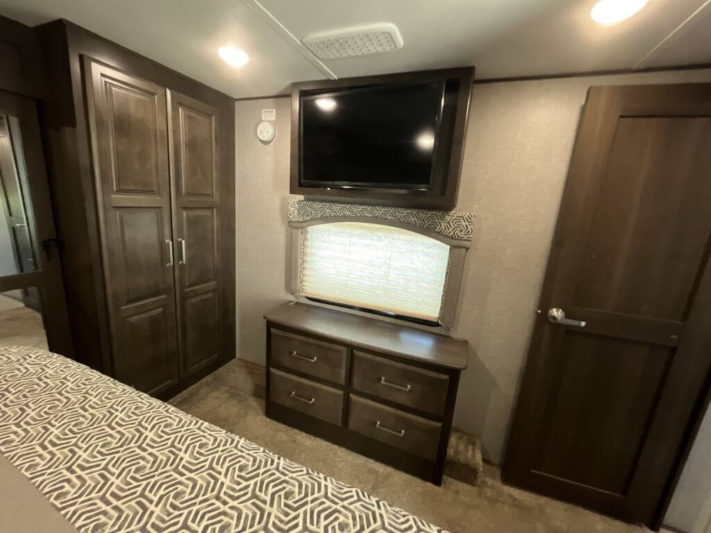 Spacious RV rental bedroom featuring a mounted TV, dresser, and large wardrobe for ample storage. Ideal for comfortable travel.. Keystone Alpine 2019