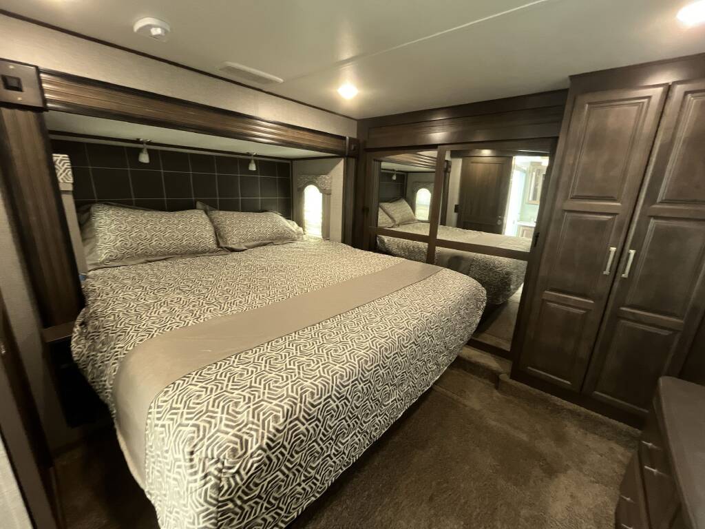 A modern, well-appointed RV rental bedroom with a large bed, patterned linens, mirrored closet, and rich wood decor.. Keystone Alpine 2019
