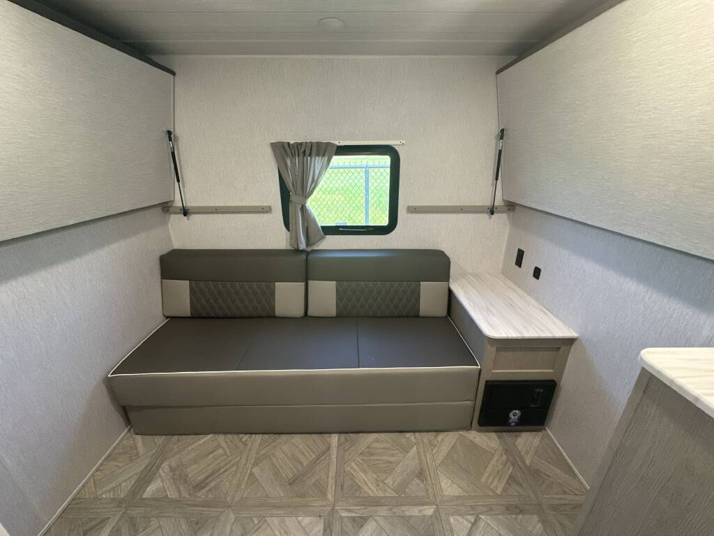 Modern RV rental interior: neutral colors, convertible couch-bed, lift-up storage, window, and light patterned floor.. Forest River Salem Cruise Lite 2024