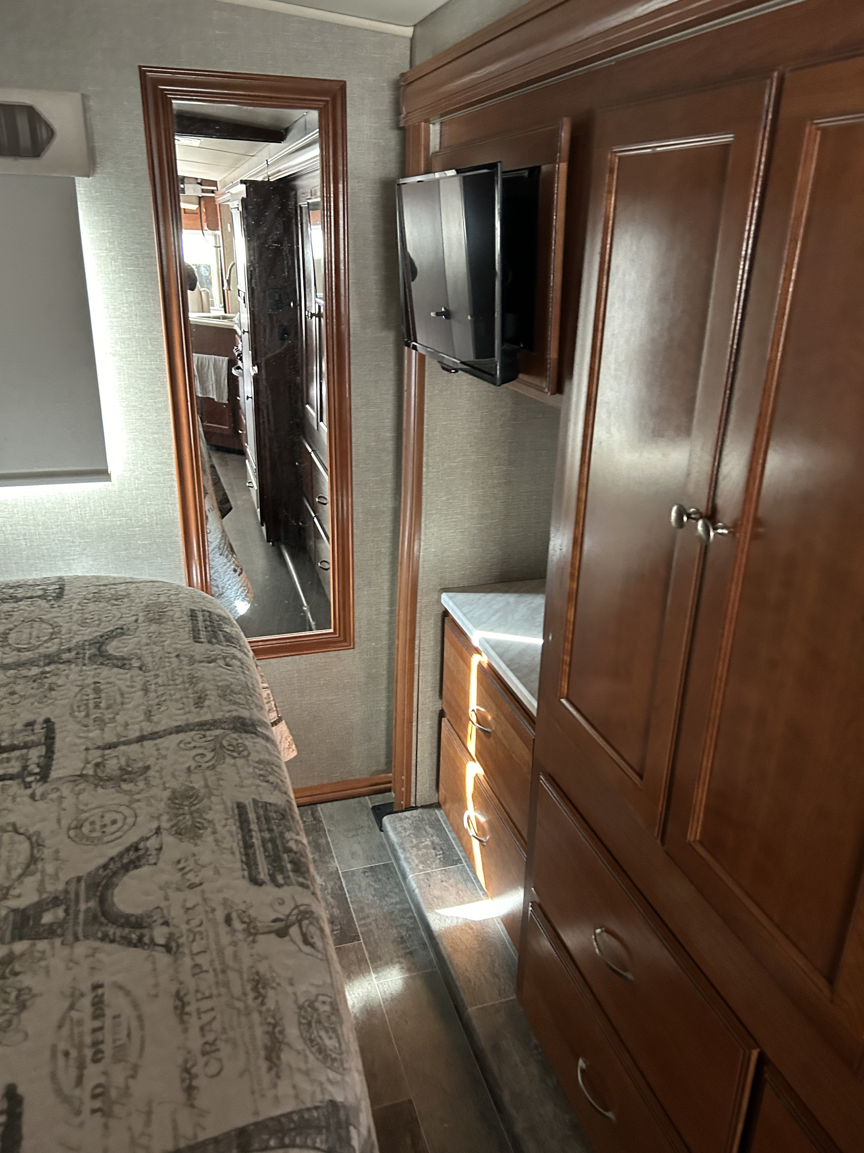 Spacious RV rental bedroom with wood cabinetry, TV, and mirror, showing ample storage and compact design.. Winnebago Vista 2019