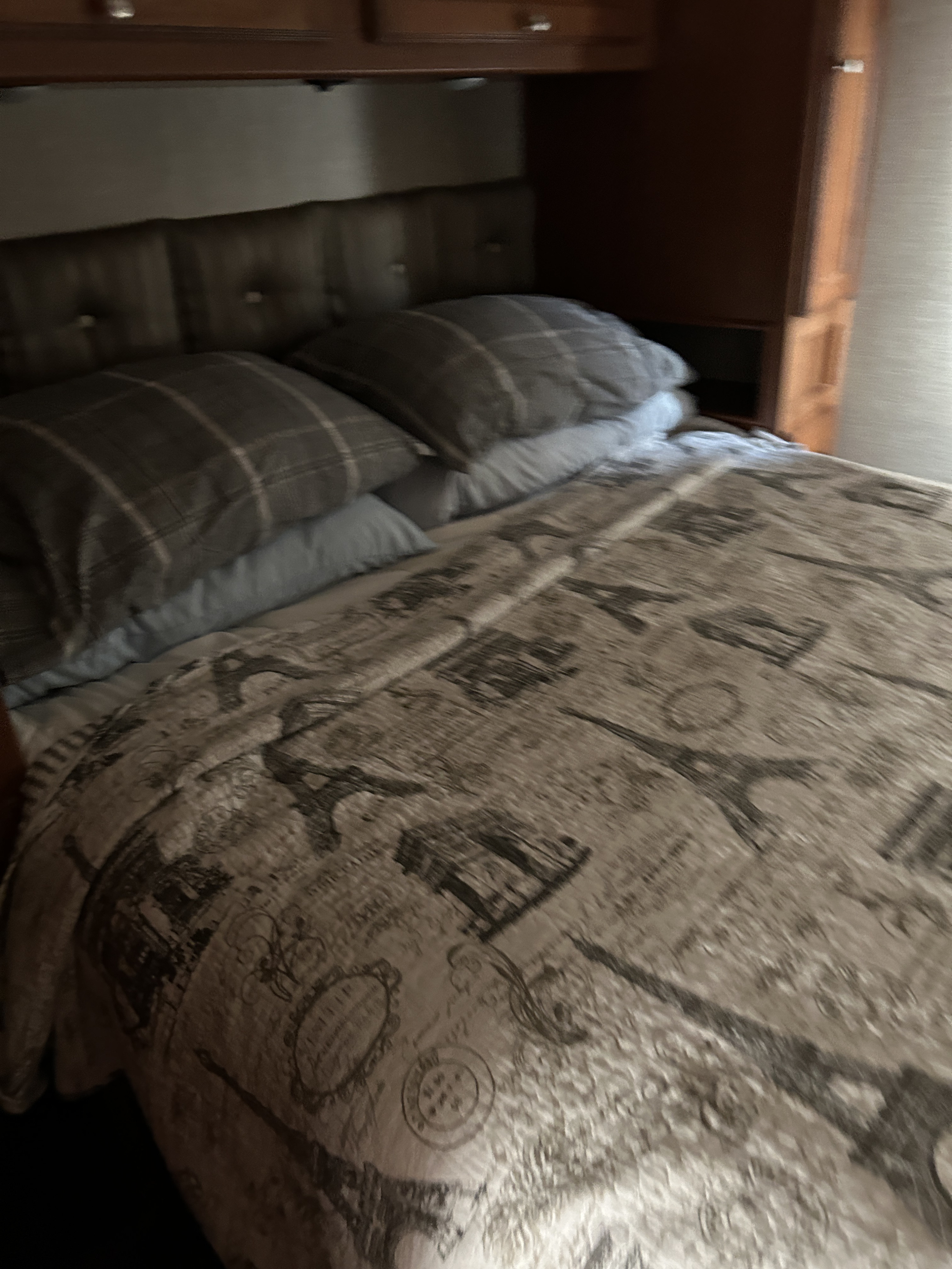 This cozy RV rental bedroom features a bed with a themed comforter & pillows under overhead wooden cabinets.. Winnebago Vista 2019