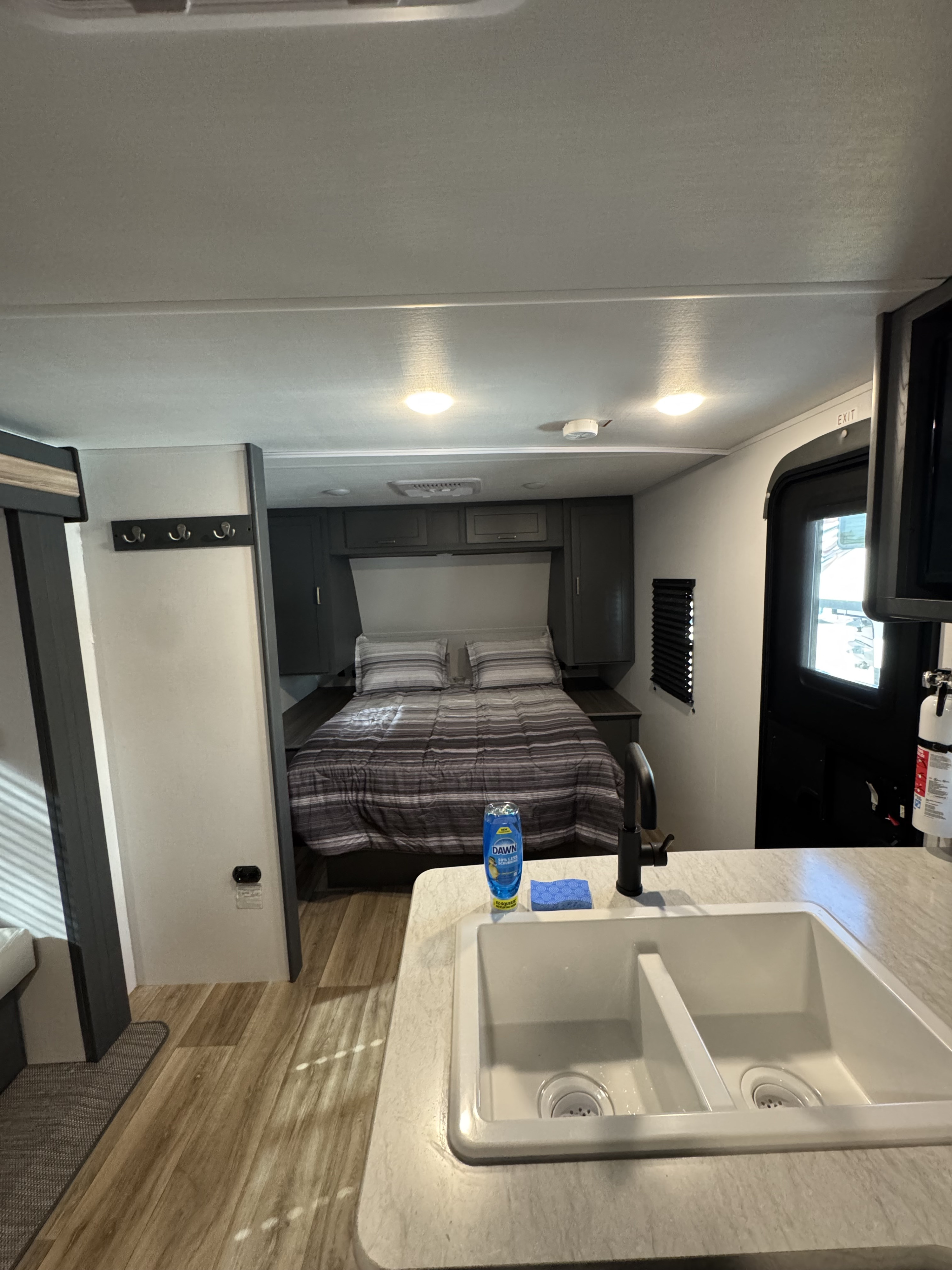 Inside an RV rental: a cozy bedroom with striped bedding and a functional kitchen area with a sink in the foreground.. Keystone RV Bullet 2024