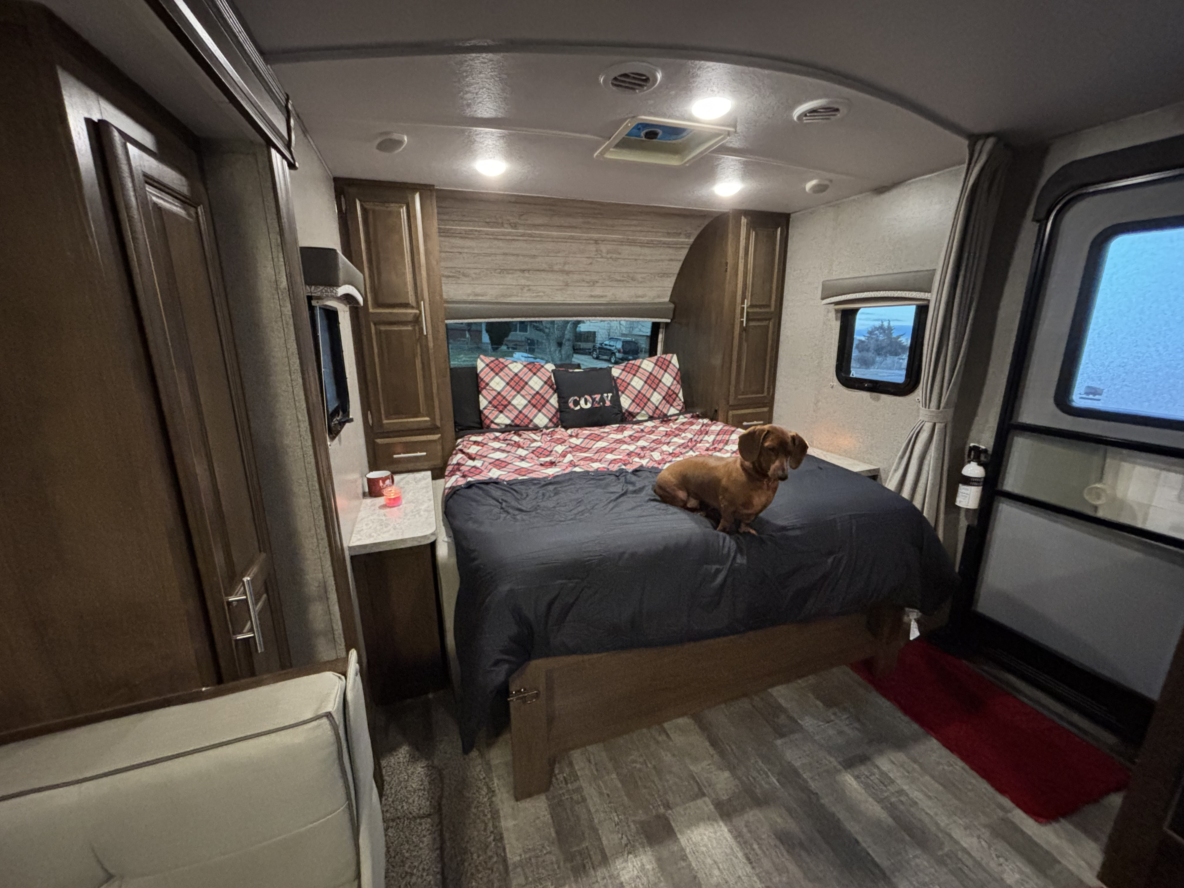 Inside a cozy RV rental bedroom: a comfy bed with plaid bedding, a dachshund, windows, and storage. Perfect for a getaway!. Forest River Rockwood Mini Lite 2019