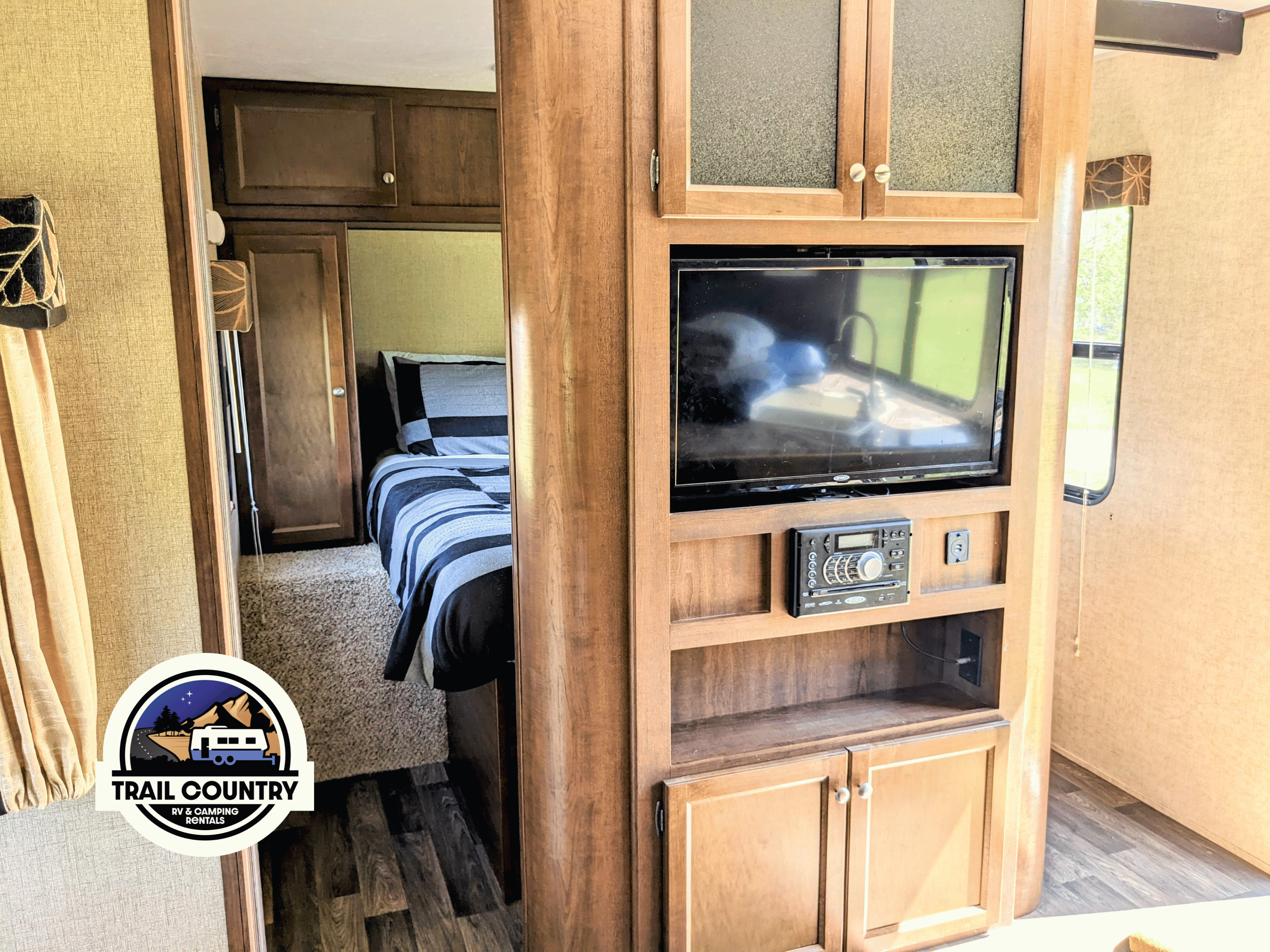 Inside this RV rental, see the cozy bedroom and living area featuring a TV, stereo, and warm wood cabinetry.. Keystone RV Hideout Luxury 31-RBDS 2016