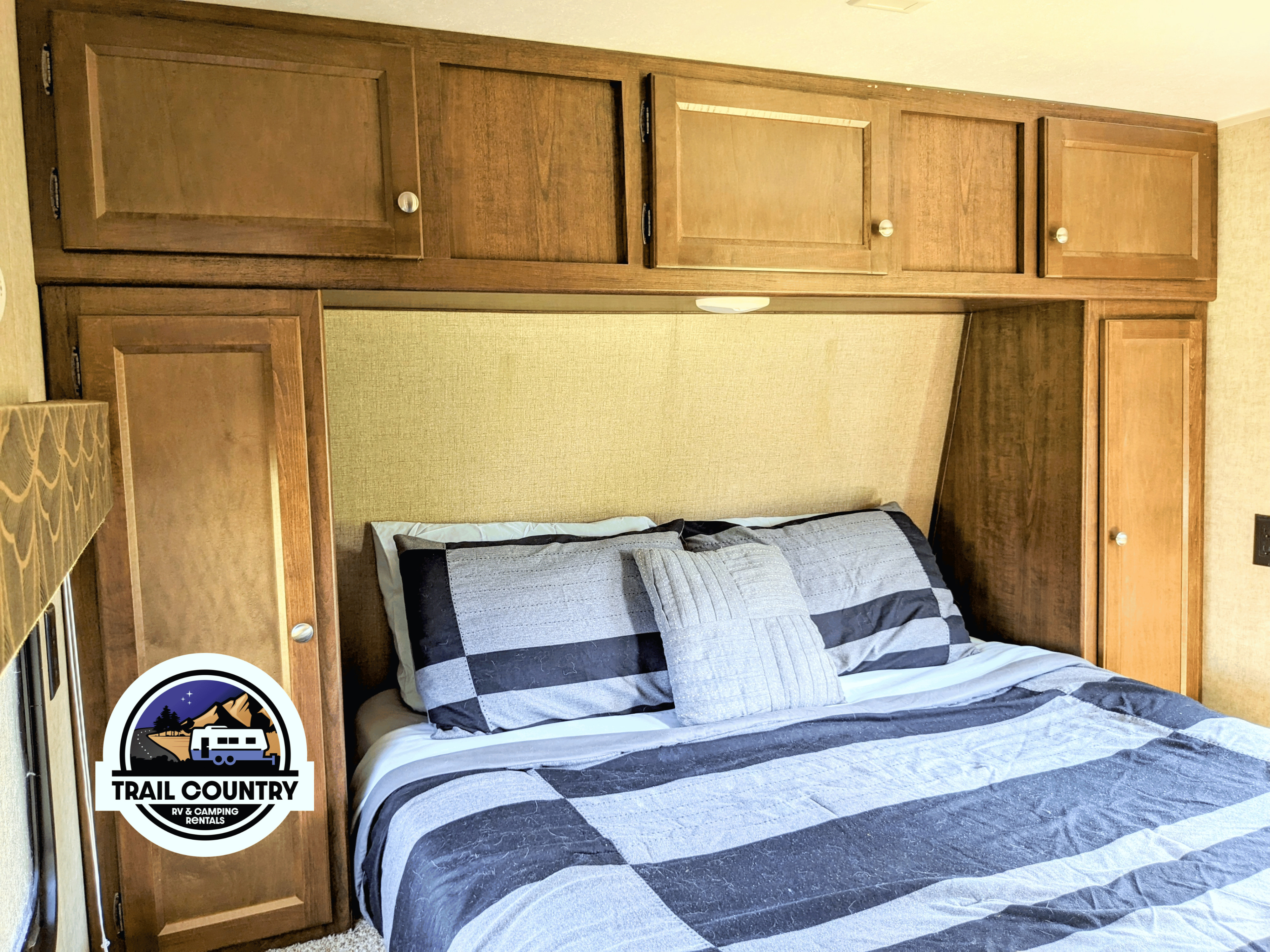 Cozy RV bedroom interior for your next RV rental adventure, featuring a comfy bed with striped bedding and wooden overhead cabinets.. Keystone RV Hideout Luxury 31-RBDS 2016