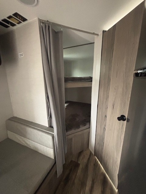 RV rental interior showing bunk beds with privacy curtain and a comfy bench seating area, perfect for family trips.. Gulf Stream Amerilite 2023