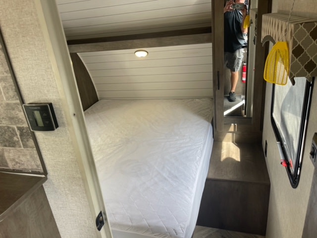 Inside an RV rental: a compact bedroom with a white bed, mirrored closet reflecting the photographer, and a wall-mounted thermostat.. Forest River Evo 2021
