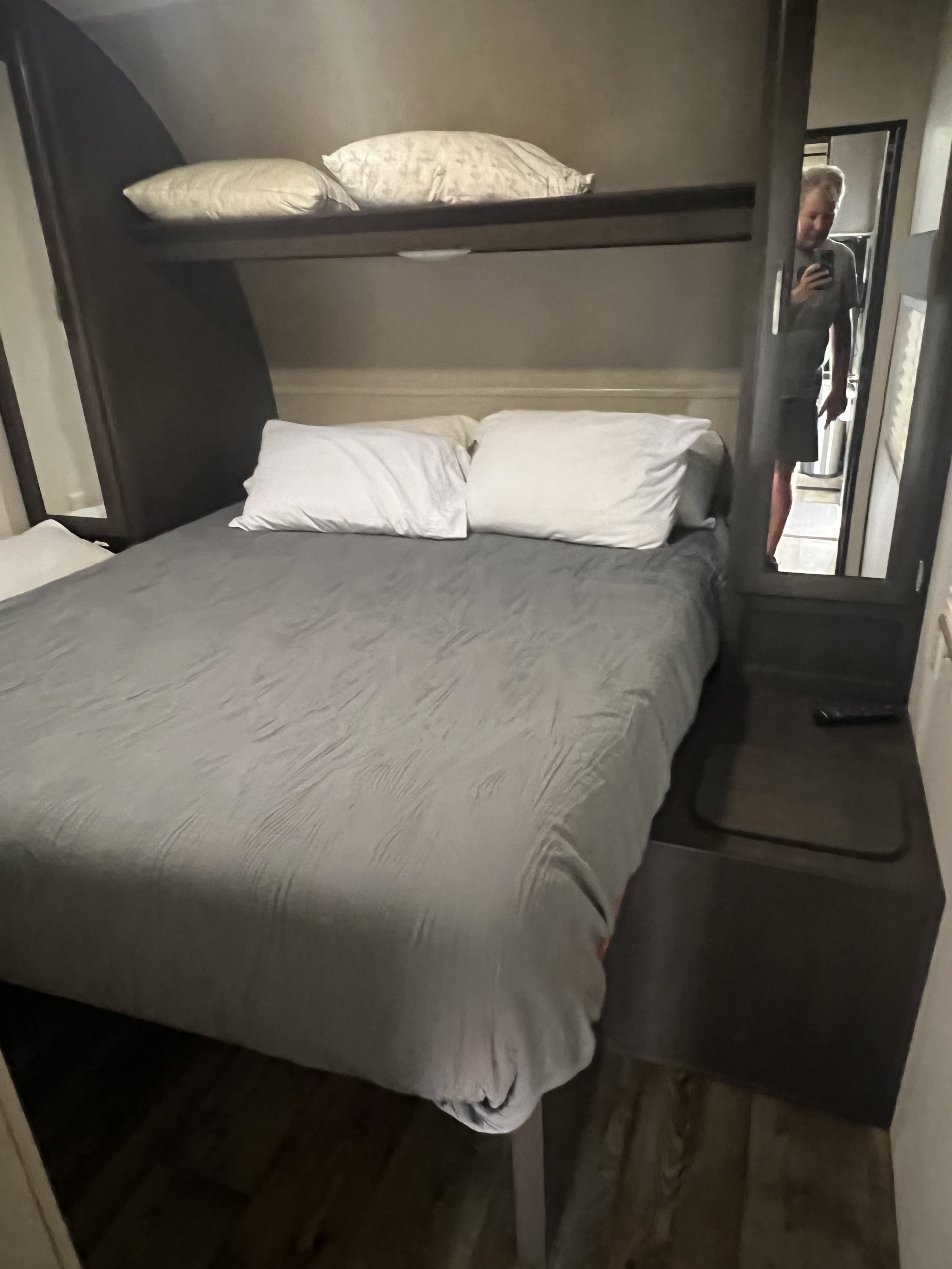 Cozy RV rental bedroom with a gray bed, white pillows, and overhead shelf. Mirror reflects person inside.. Forest River Sandstorm 2017