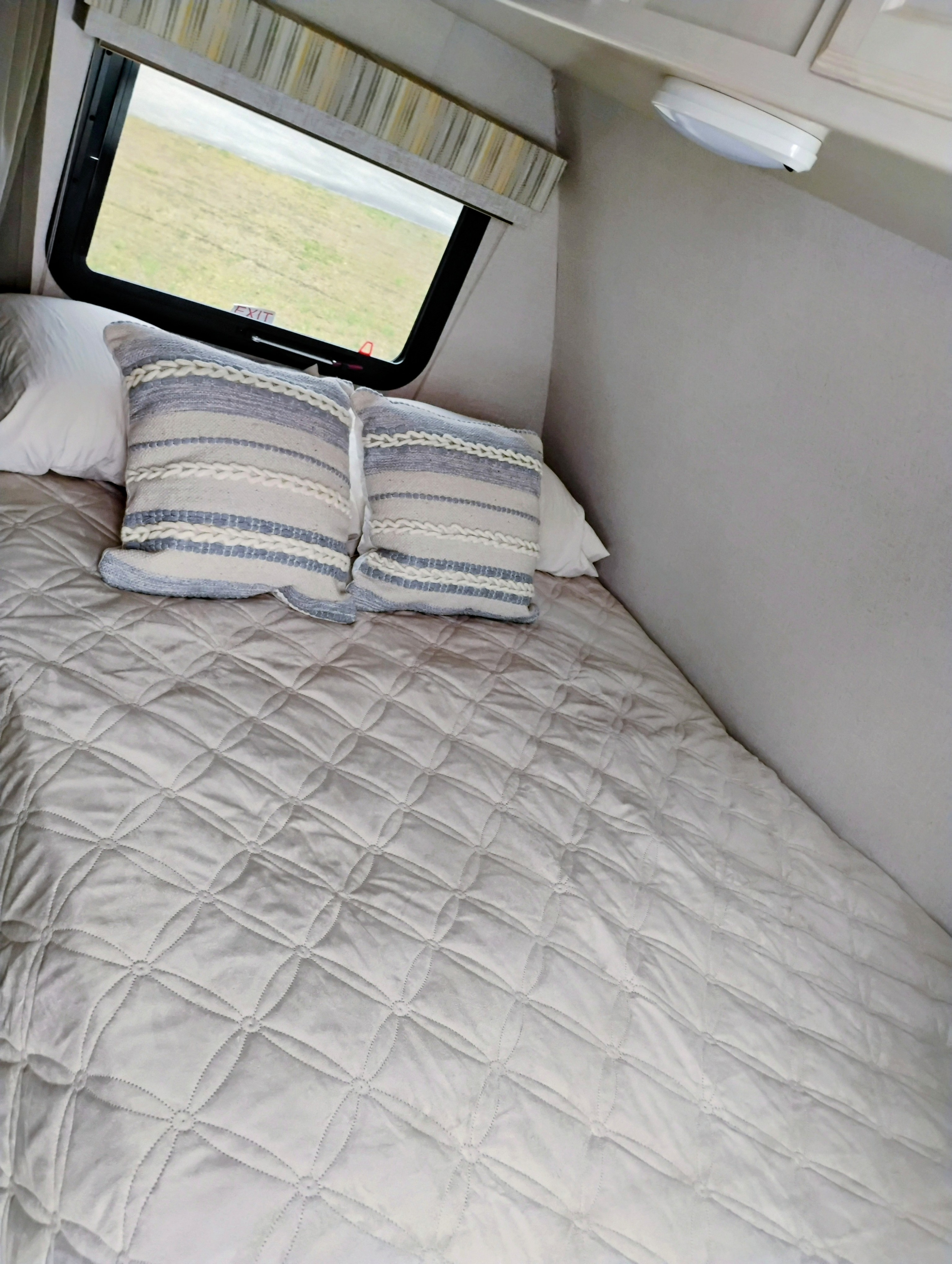 Cozy RV rental bedroom with a quilted bed, decorative pillows, and a window showing a grassy field outside.. Winnebago Towables Micro Minnie 2018