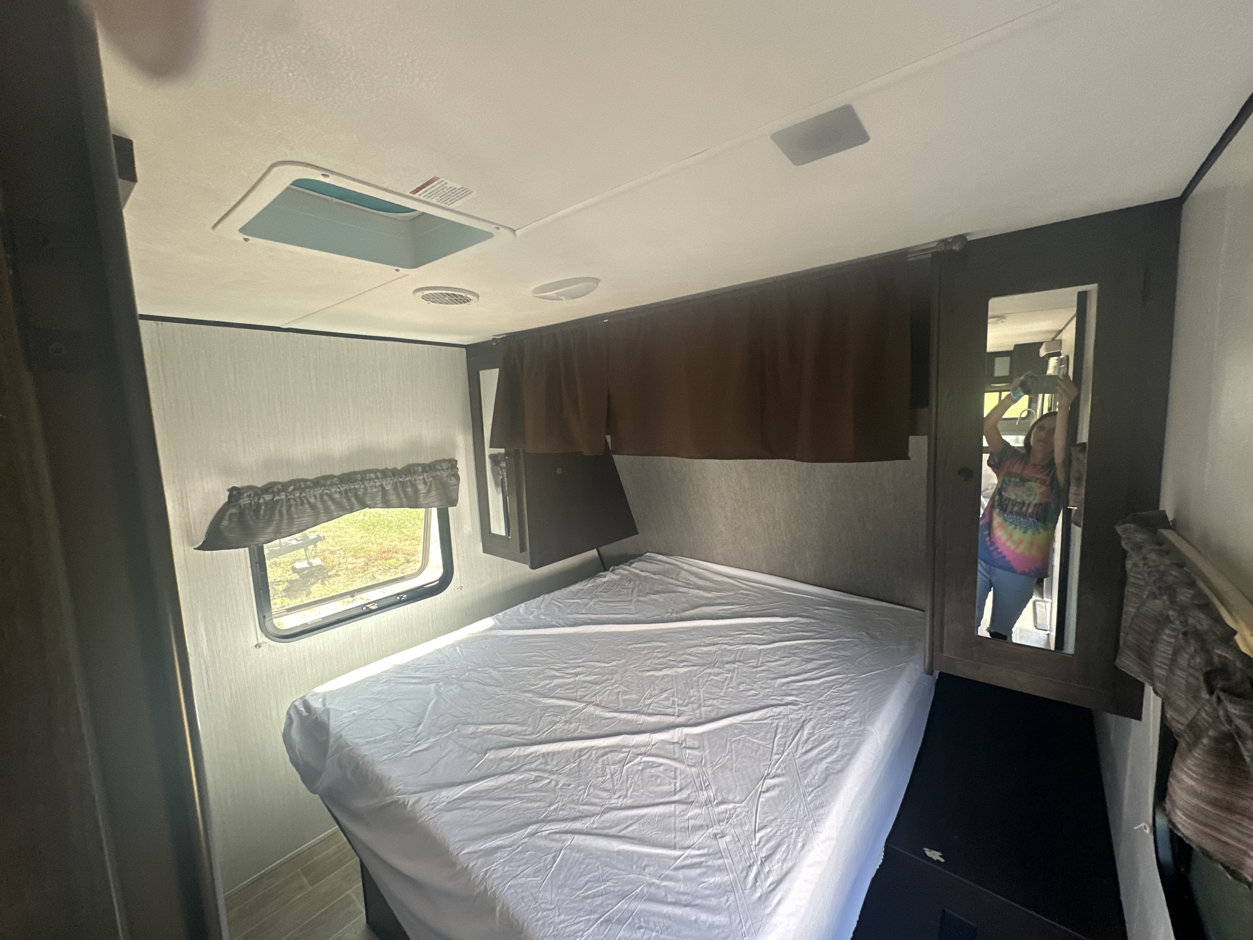 Spacious RV rental bedroom featuring a bed with white sheets, window with outdoor view, and a mirrored wardrobe.. Heartland RVs Trail Runner 2022