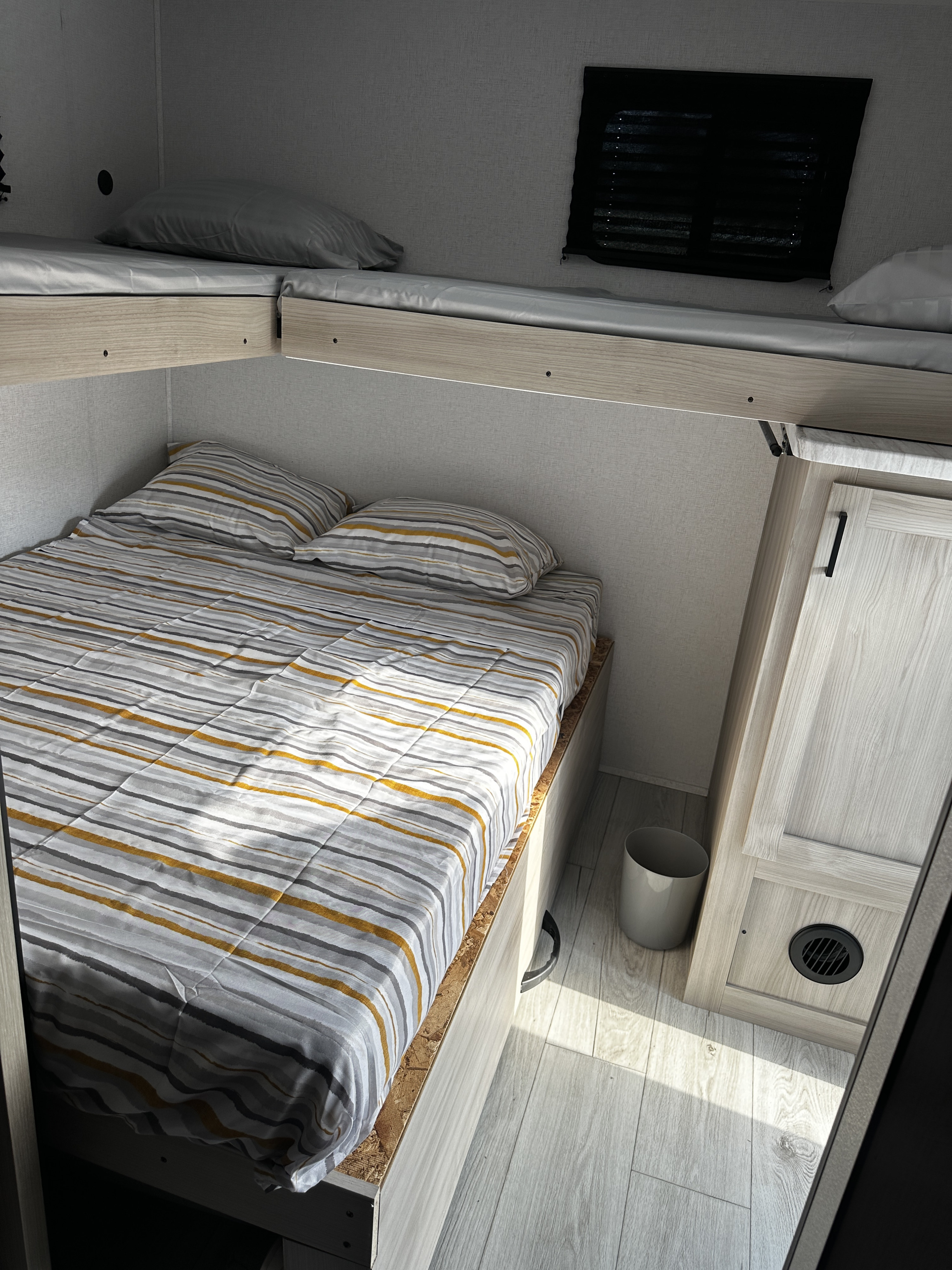 Inside an RV rental: a modern bedroom with a lower bed featuring striped bedding and two simple upper bunk beds, optimized for compact living.. Forest river Silver lake 2025