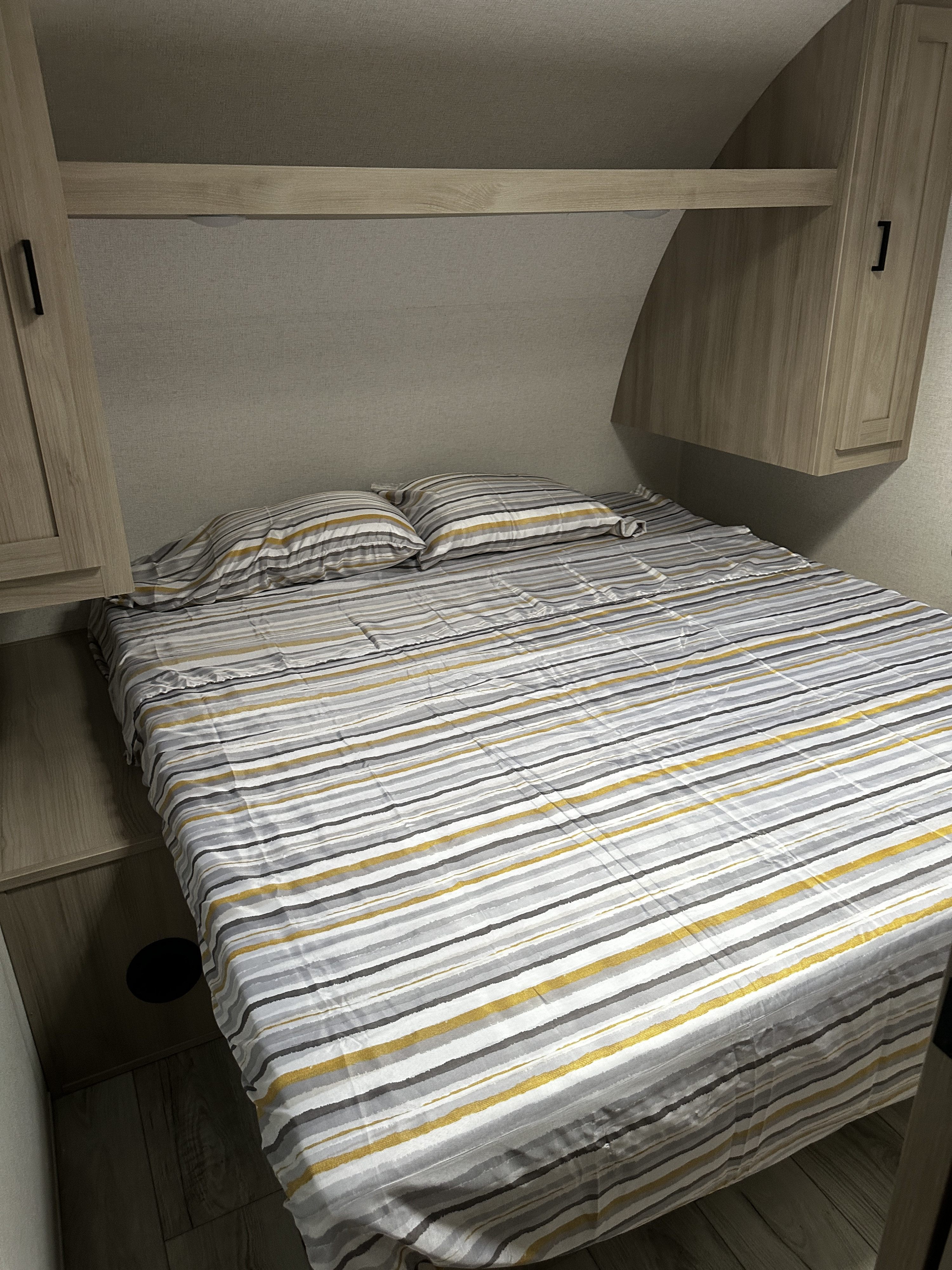 Cozy striped bed with grey, white, and yellow sheets inside an RV rental, featuring built-in cabinets and a shelf above.. Forest river Silver lake 2025