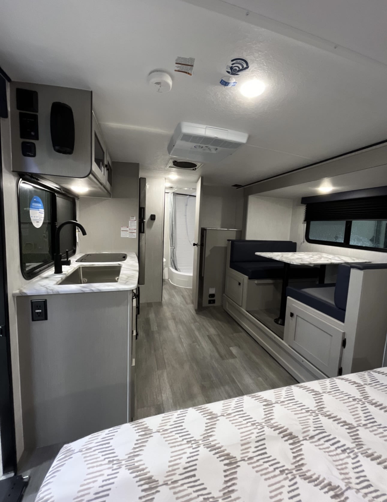 Modern RV rental interior: kitchen with sink, dinette, and bed. A shower is visible in the background, great for road trips.. Coachmen Apex 2022