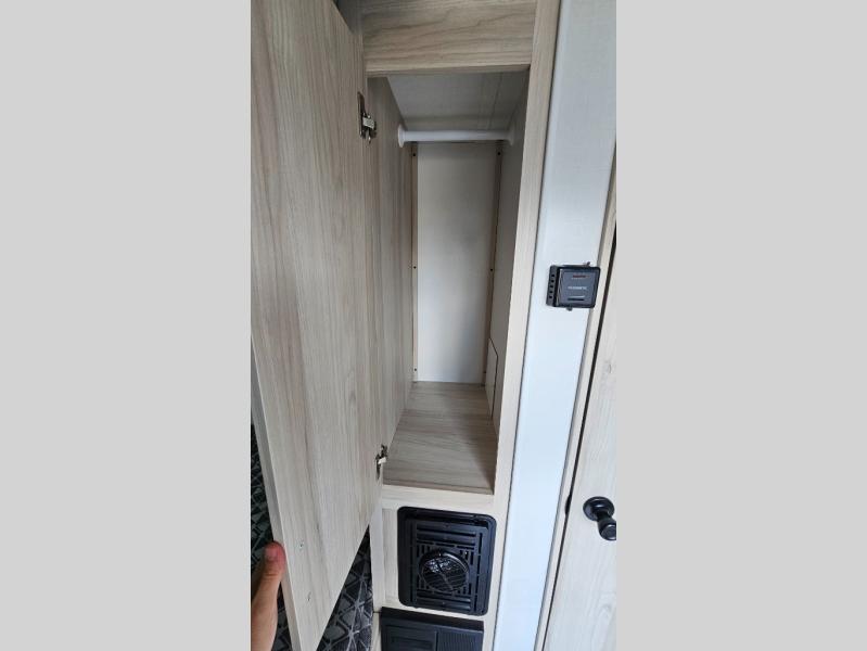 This RV rental features an open wardrobe with a hanging rod, a Dometic thermostat, and a heating vent below.. Winnebago Hike 100 2023