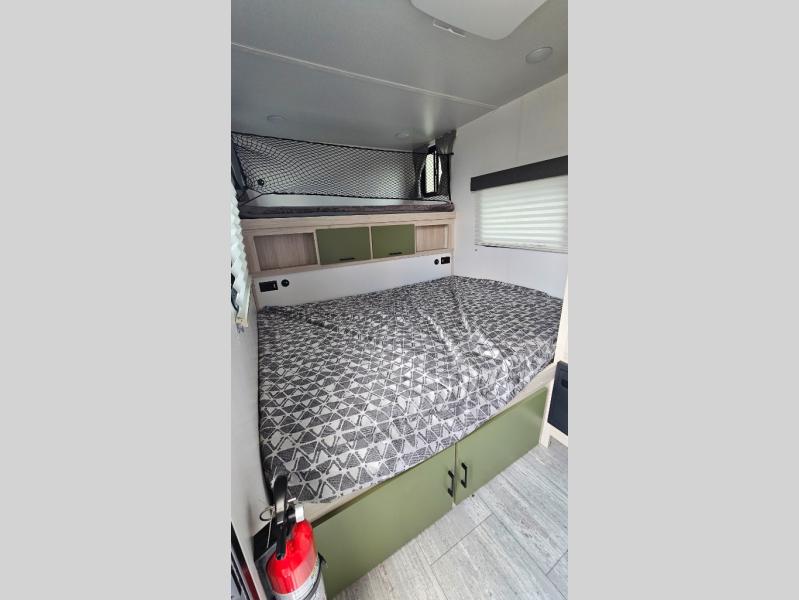 RV rental bedroom featuring a patterned lower bed, upper bunk, and green storage. Fire extinguisher visible.. Winnebago Hike 100 2023