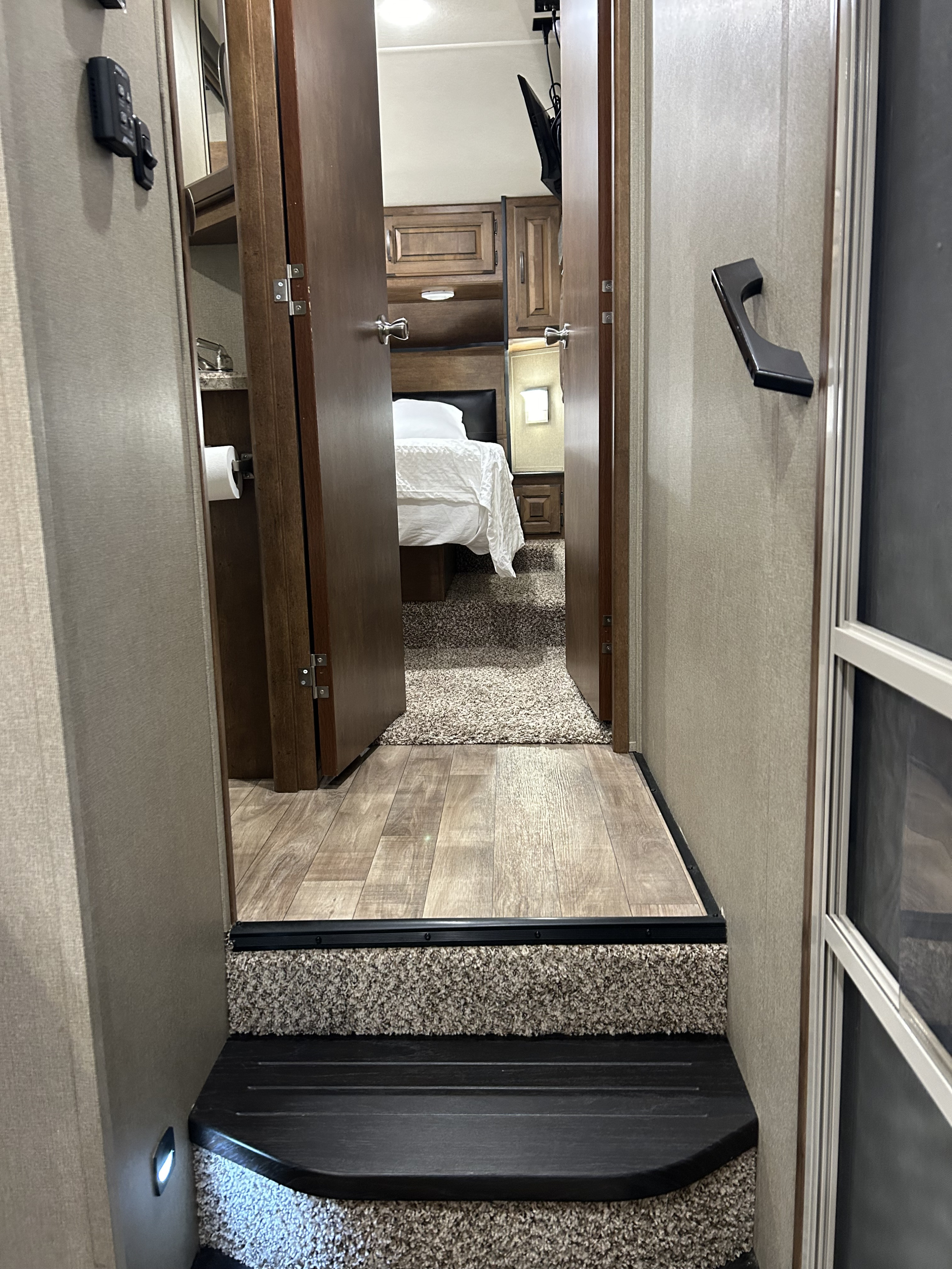 Inside an RV rental: Steps lead to a cozy bedroom through open doors. Features wood-look and carpeted floors, and interior controls.. Grand Design Reflection 2017