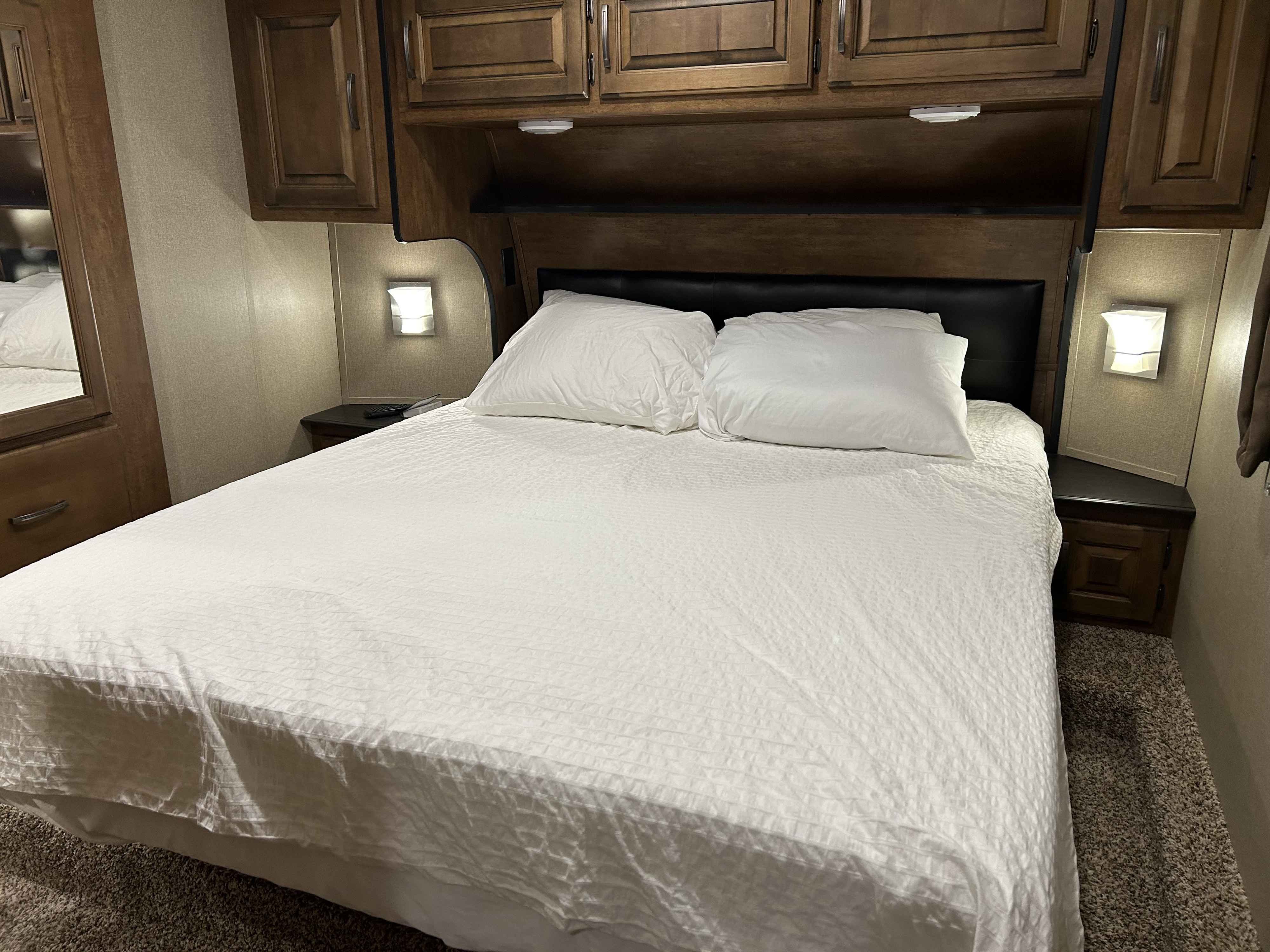 Cozy RV rental bedroom featuring a neatly made bed with white bedding, built-in wooden cabinets, and functional wall lights.. Grand Design Reflection 2017
