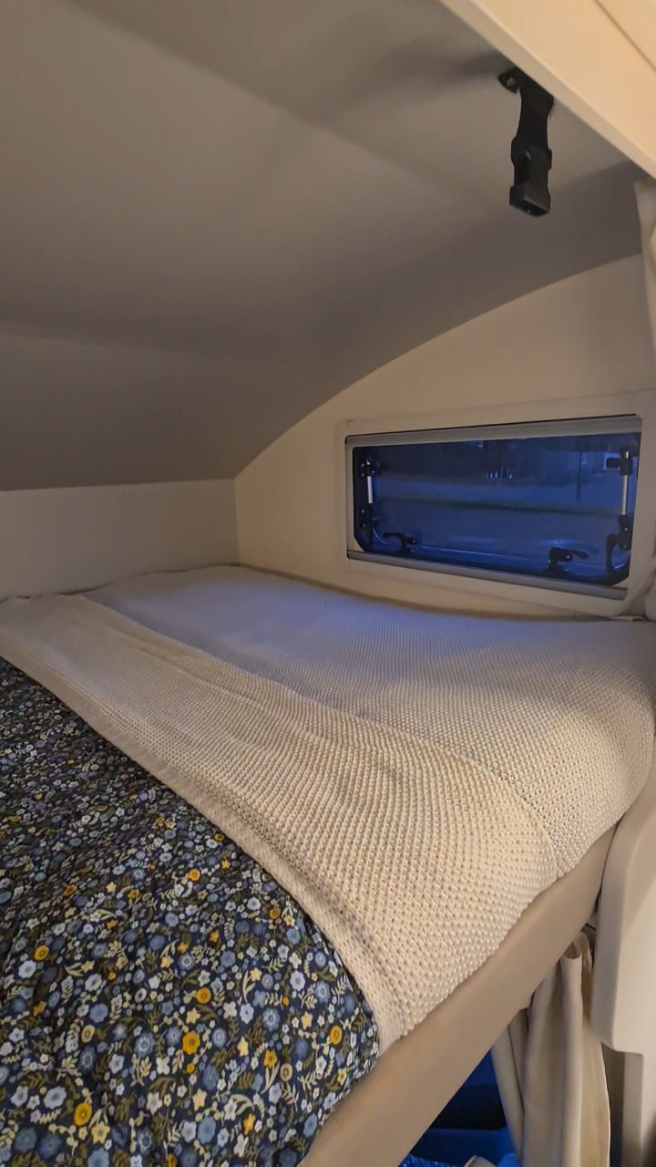 Cozy RV rental bedroom with patterned duvet, knitted blanket, and window view. Ideal for travel comfort.. Ford Transit Rimor Evo Sound 7 2022