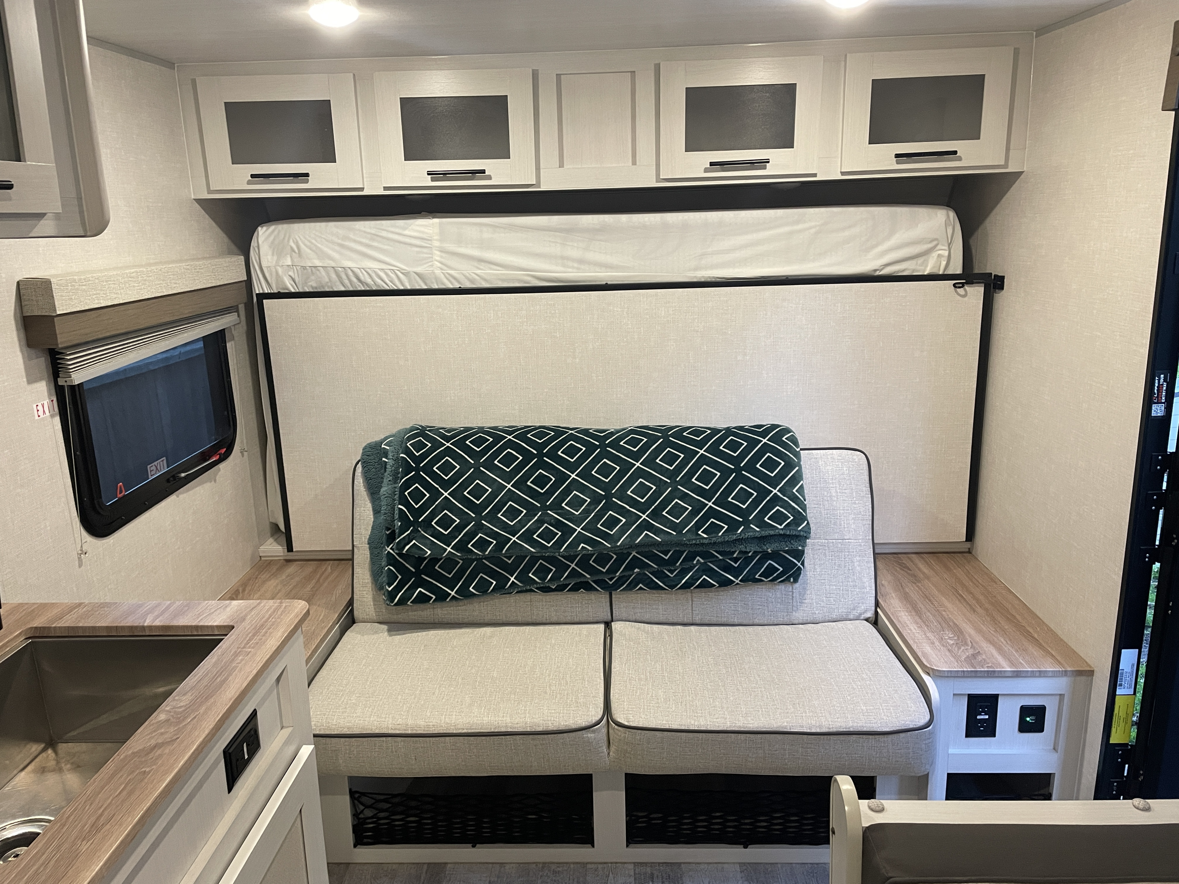 Inside an RV rental: versatile living space with sofa seating, a pull-down bed, overhead cabinets, and a compact kitchen area.. No Boundaries NoBo 19.3 Essentials Only 2024