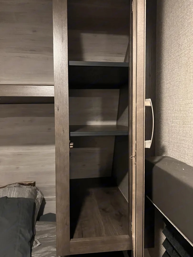 Open, narrow wood-grain cabinet with shelves inside an RV rental bedroom, perfect for compact storage.. Jayco Jay Flight SLX 2021
