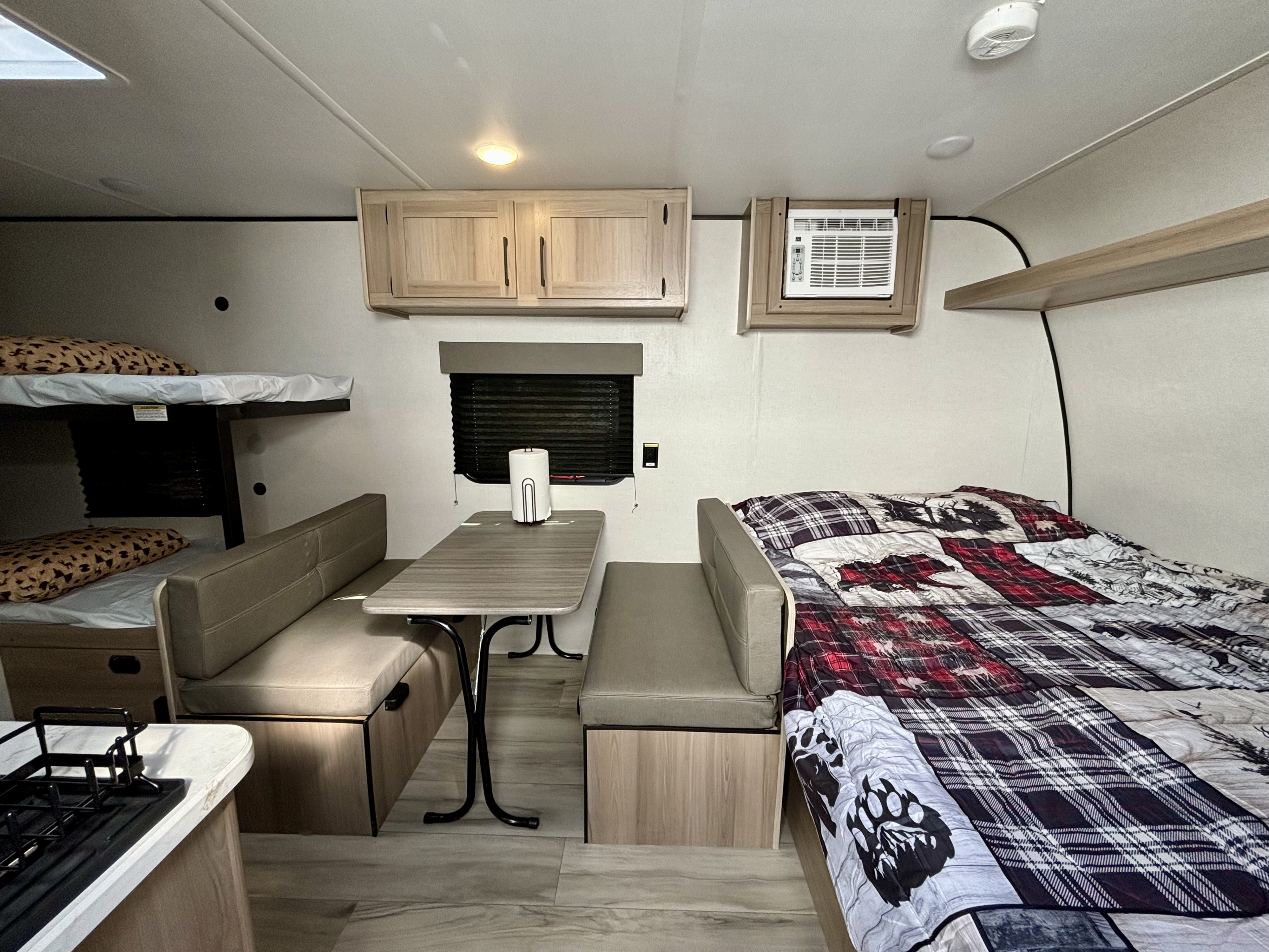 Inside an RV rental, showing bunk beds, a dinette, kitchen counter, an AC unit, and a main bed with patterned bedding.. Coleman 17B 2025