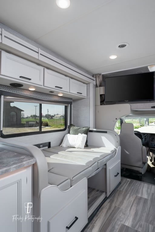 Modern RV rental interior: convertible dinette bed, ample overhead storage, & mounted TV for comfortable travel.. Thor Four Winds 2021