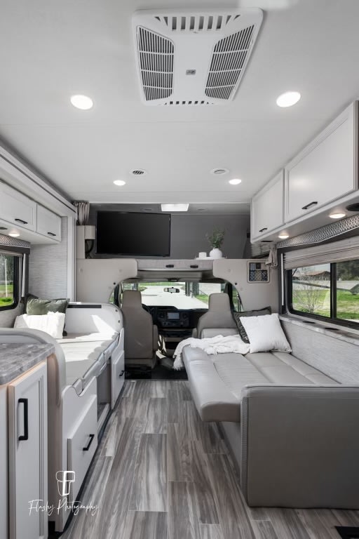 Spacious, modern RV rental interior with light wood floors, grey seating, and a TV, showcasing comfortable travel living.. Thor Four Winds 2021