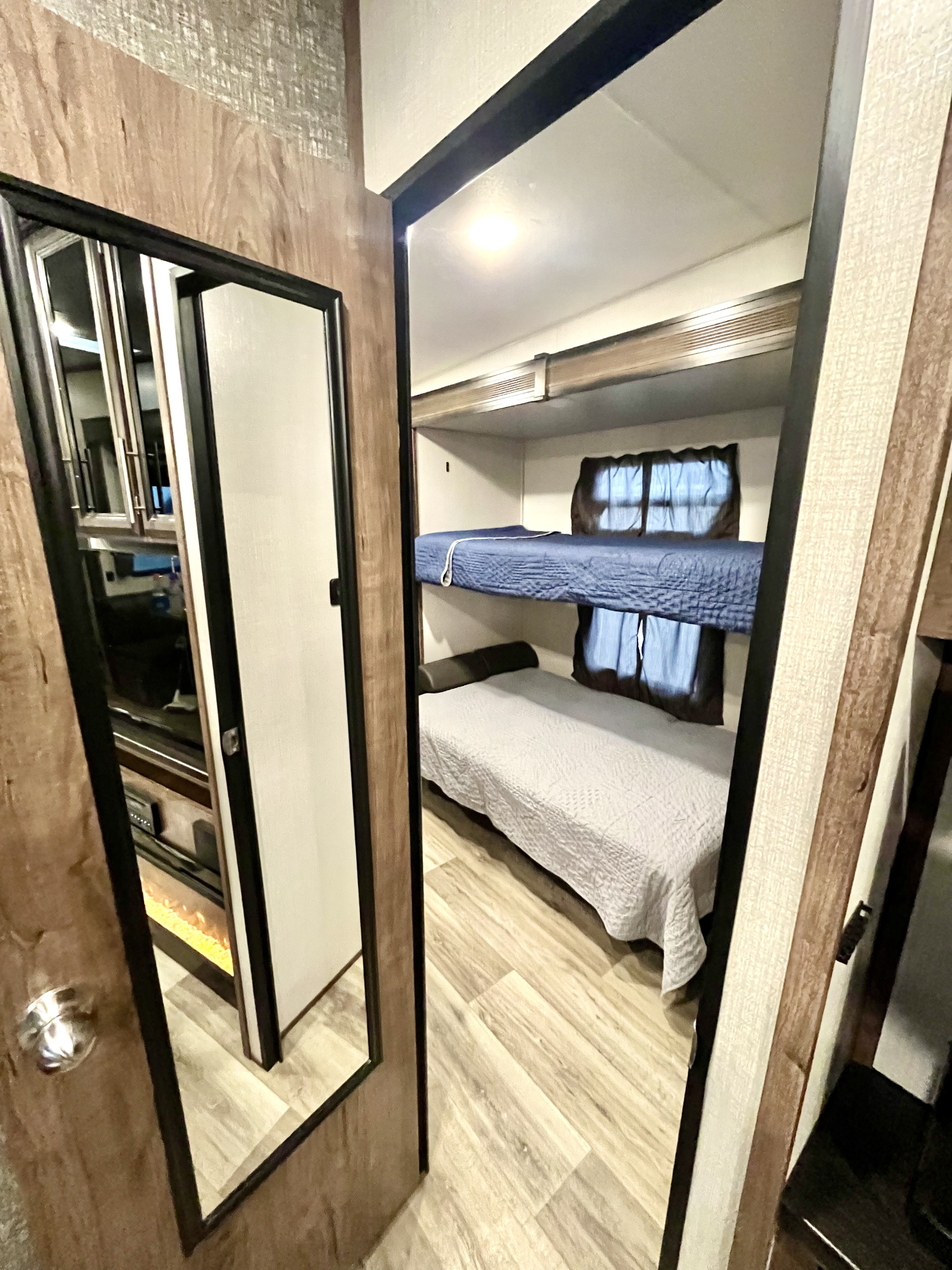 Inside an RV rental: view of a two-tier bunk bed bedroom with blue and grey comforters, and light wood flooring.. K-Z Manufacturing Durango 2021
