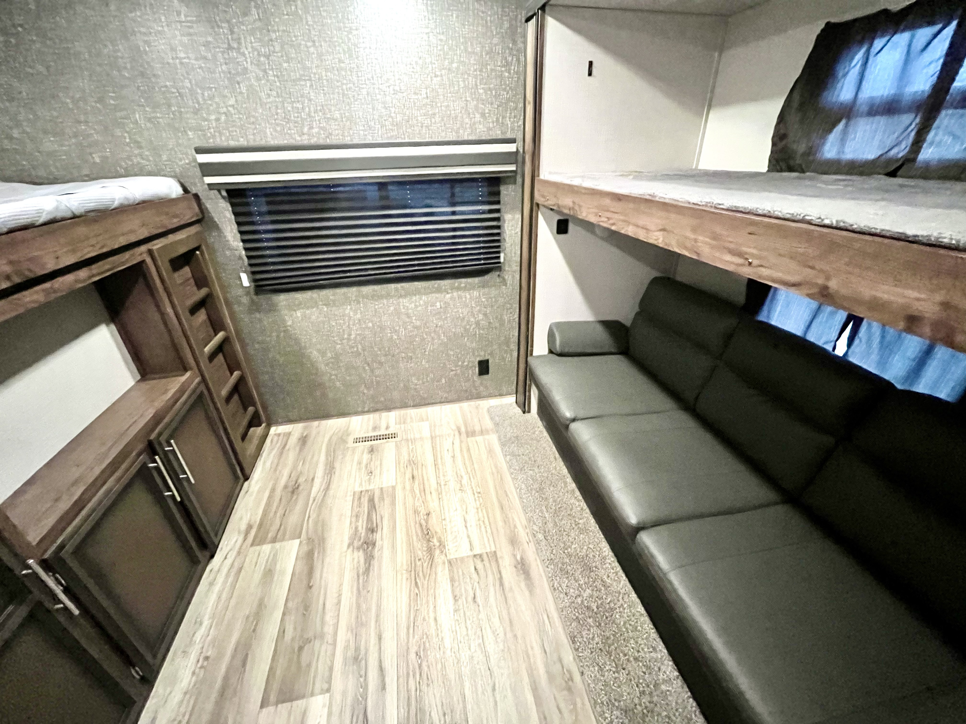 An RV rental interior shows two bunk beds, a dark sofa, and wooden storage. Light wood floors enhance the functional space.. K-Z Manufacturing Durango 2021