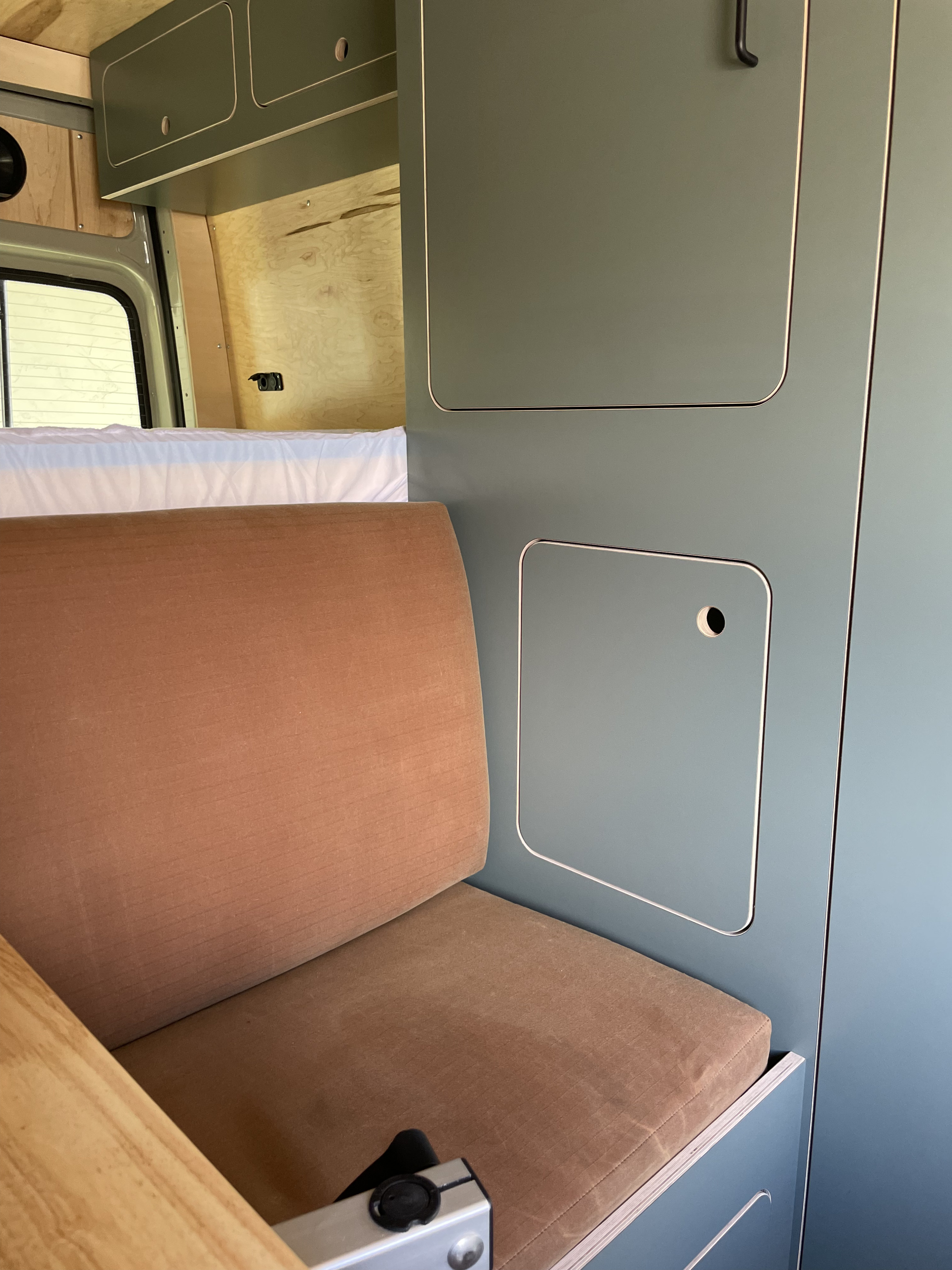 Modern camper van interior features a comfy bench seat, sleeping area, and clever sage green storage for your RV rental.. VanCraft VanCraft Class B 2023