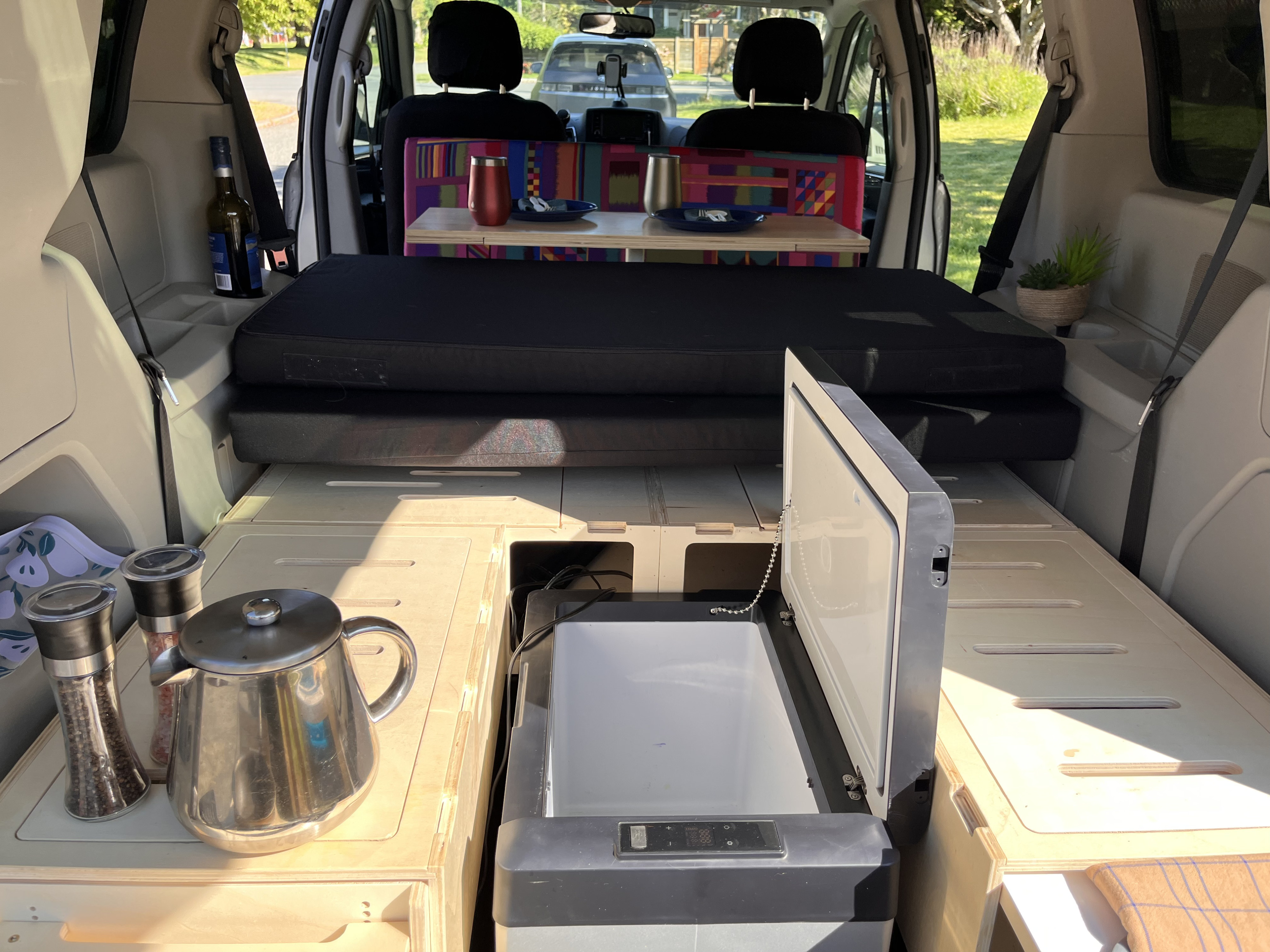 RV rental: Inside a converted van with a bed, wooden storage, cooler, and dining table set for two.. Dodge Grand Caravan 2013