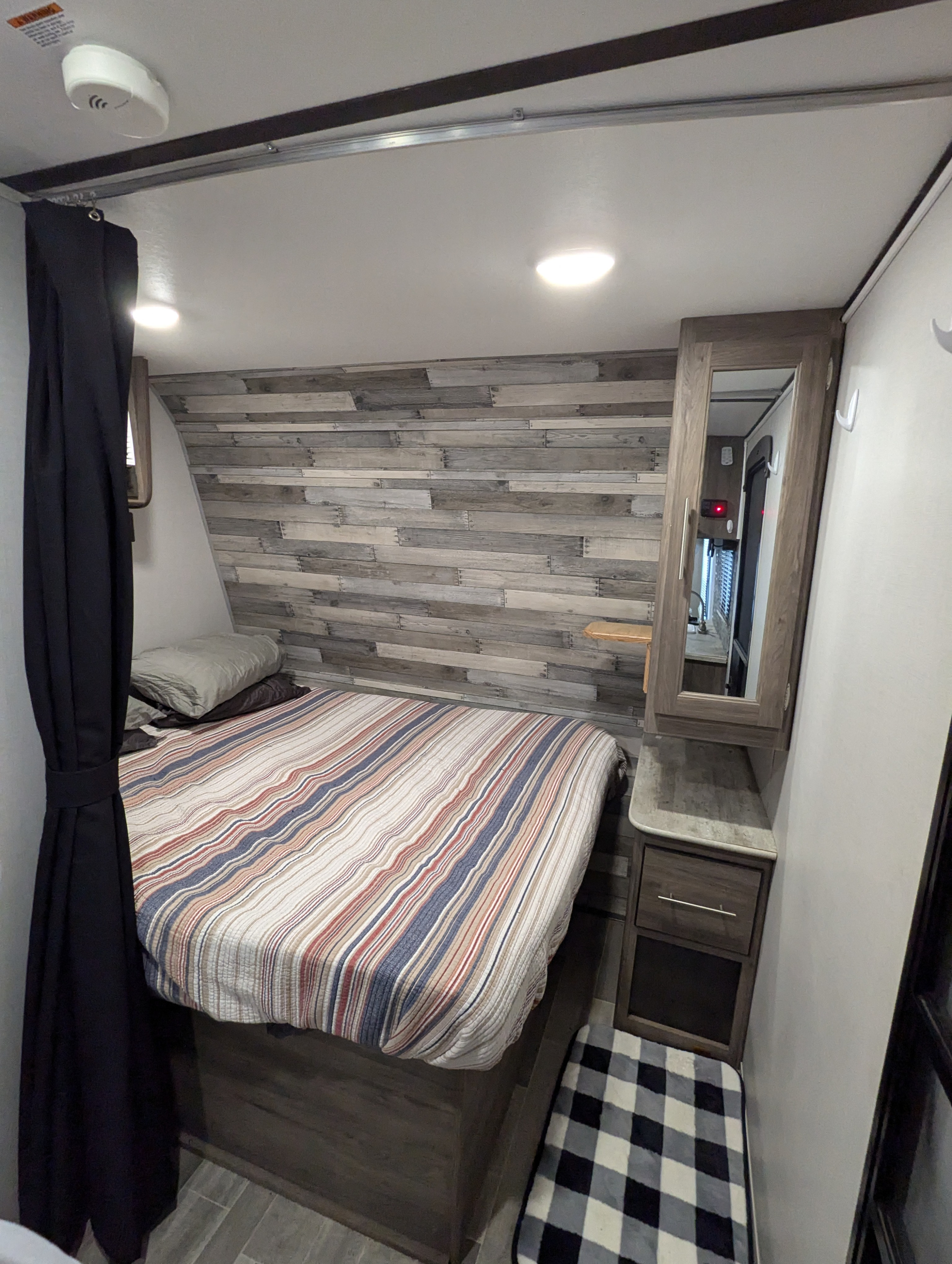 This RV rental offers a well-appointed bedroom with a striped bed, stylish wood-paneled wall, and practical storage solutions.. Crossroads RV Zinger Lite 2020