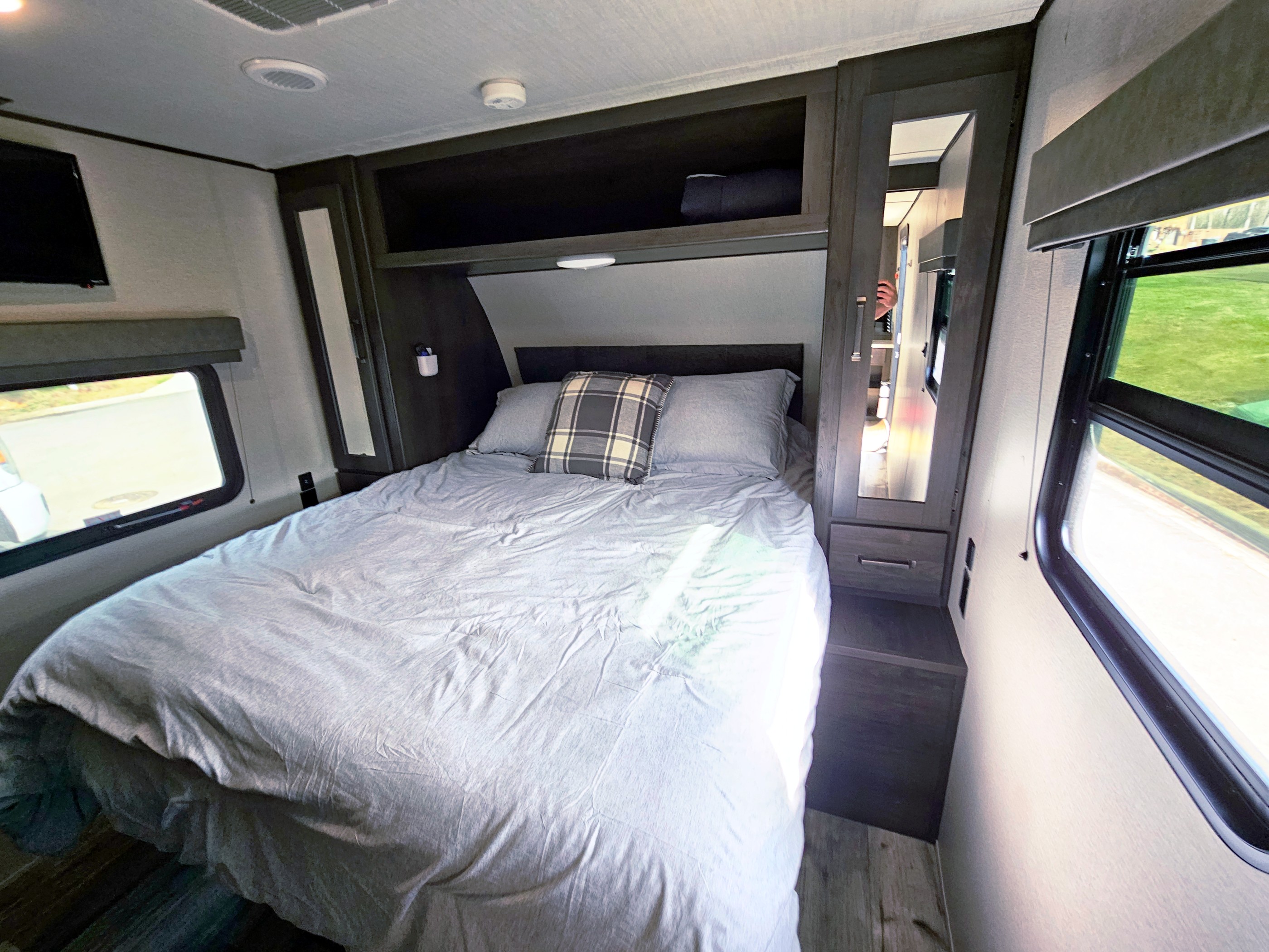 Cozy RV rental bedroom interior with a comfortable bed, overhead cabinets, and windows. Ideal for travel.. Grand Design Transcend Xplor 2023