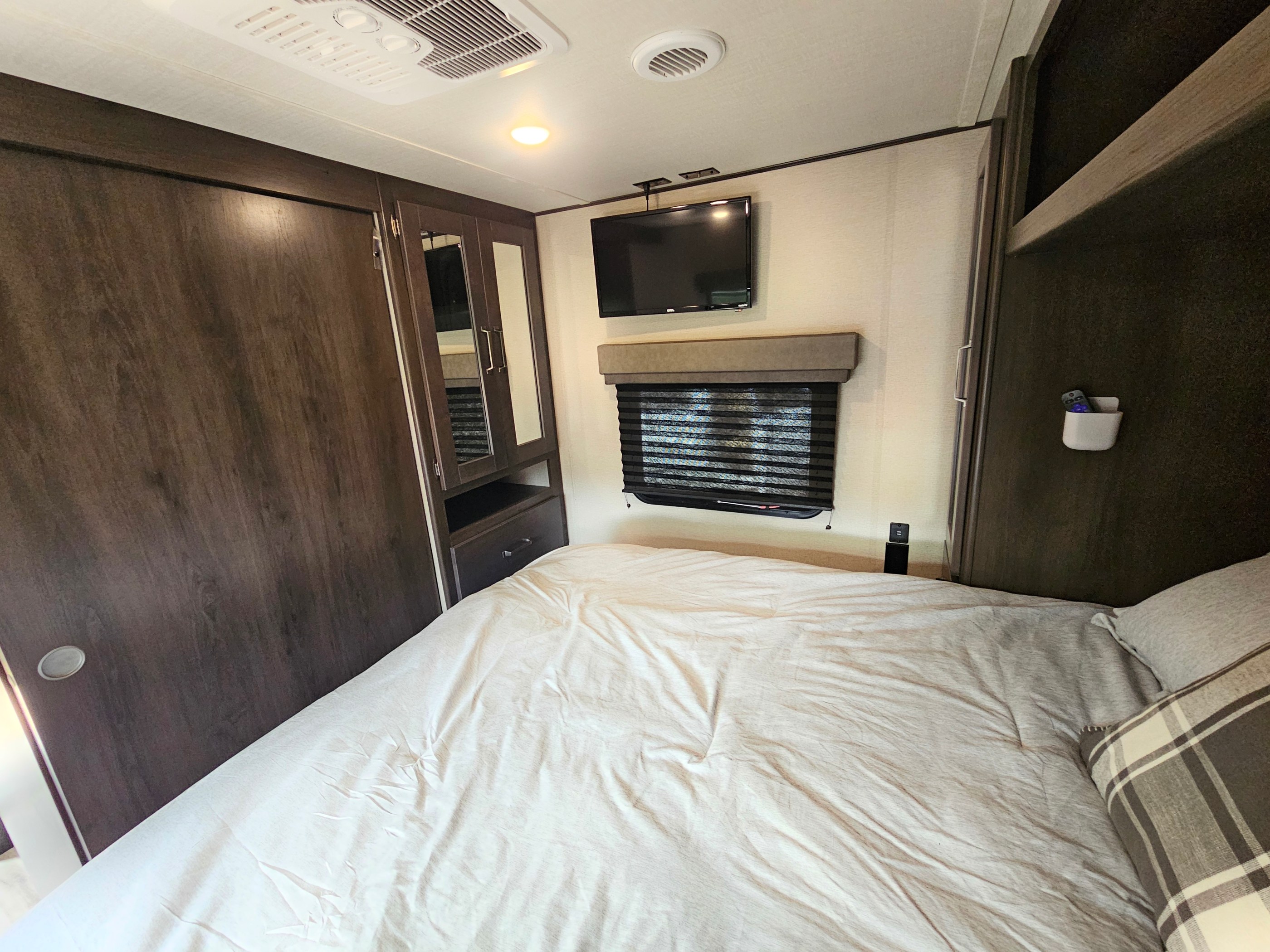 Cozy RV rental bedroom: features include a comfortable bed, wall-mounted TV, window blind, and built-in mirrored wardrobe.. Grand Design Transcend Xplor 2023